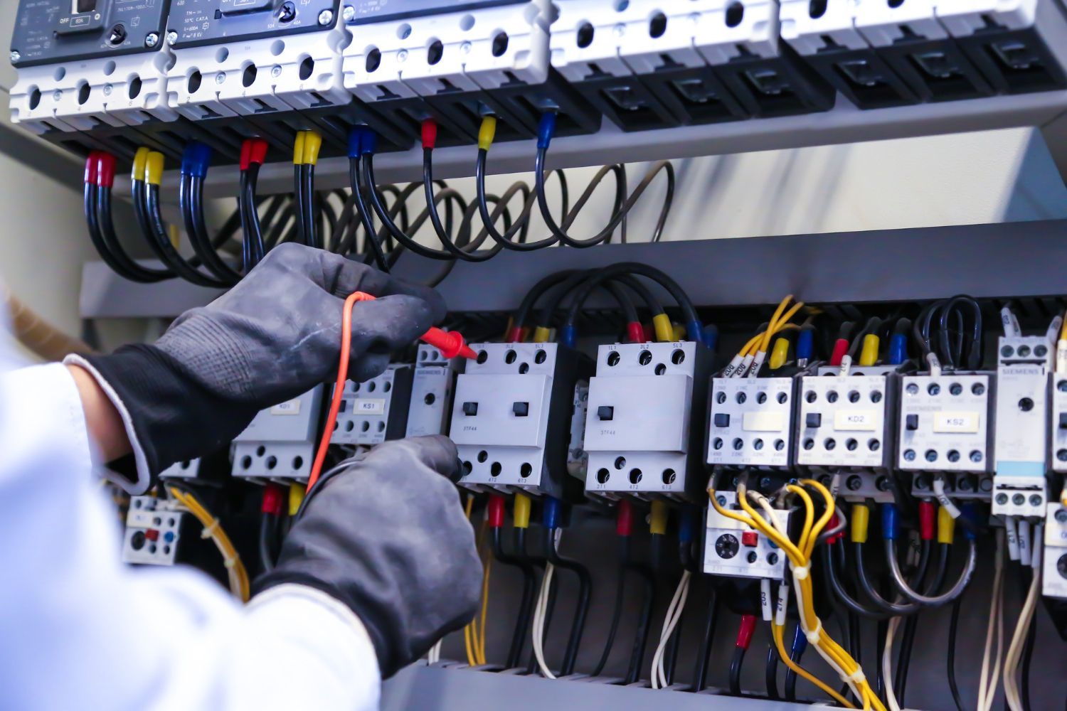 Technician wiring an electrical control panel with circuit breakers and colored cables