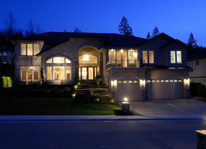 Illuminated suburban house at dusk with arched windows and a three-car garage