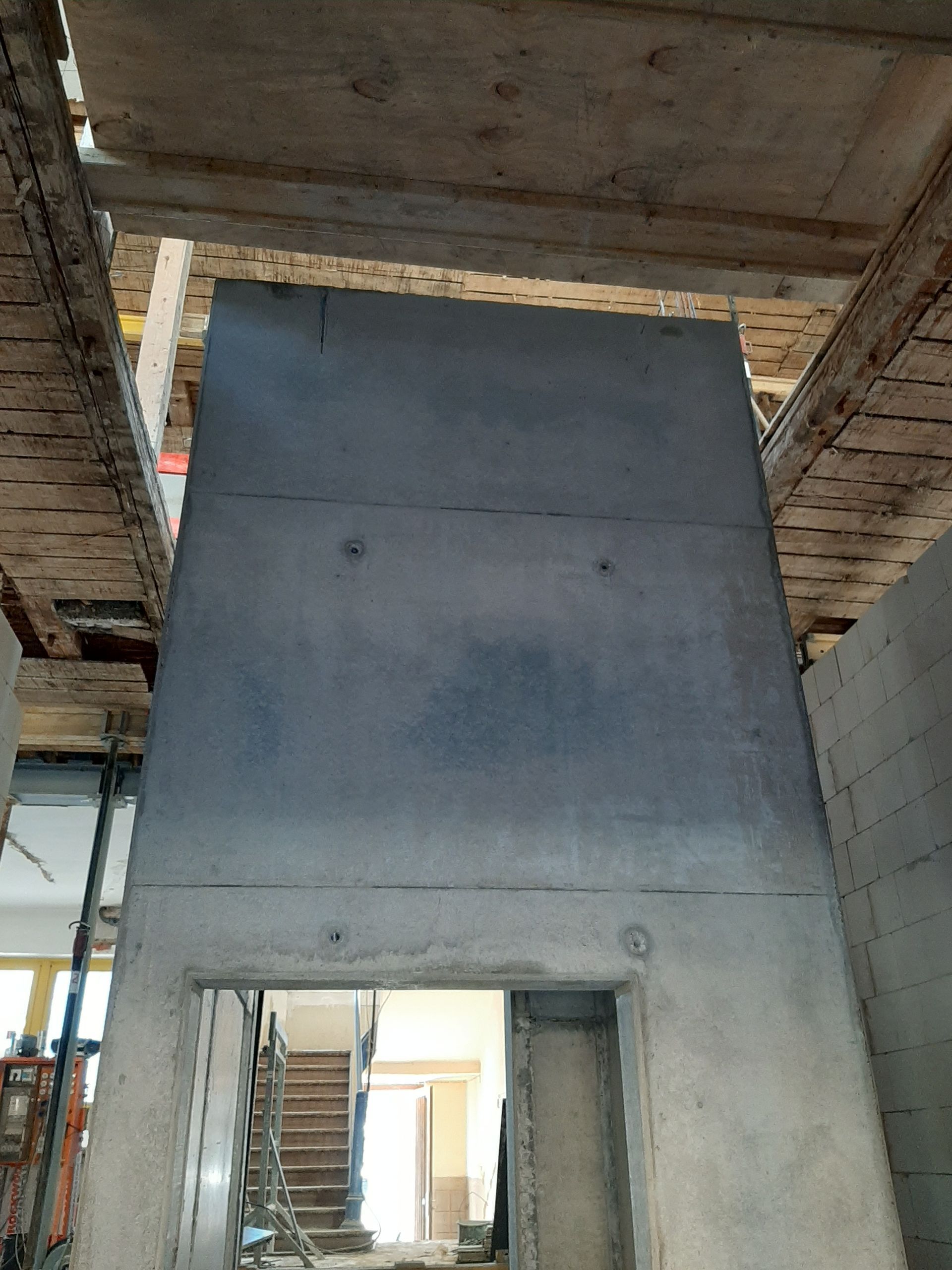 Eine hohe, vertikale Betonkonstruktion in einer Baustellenhalle mit einer rechteckigen Öffnung an der Basis.