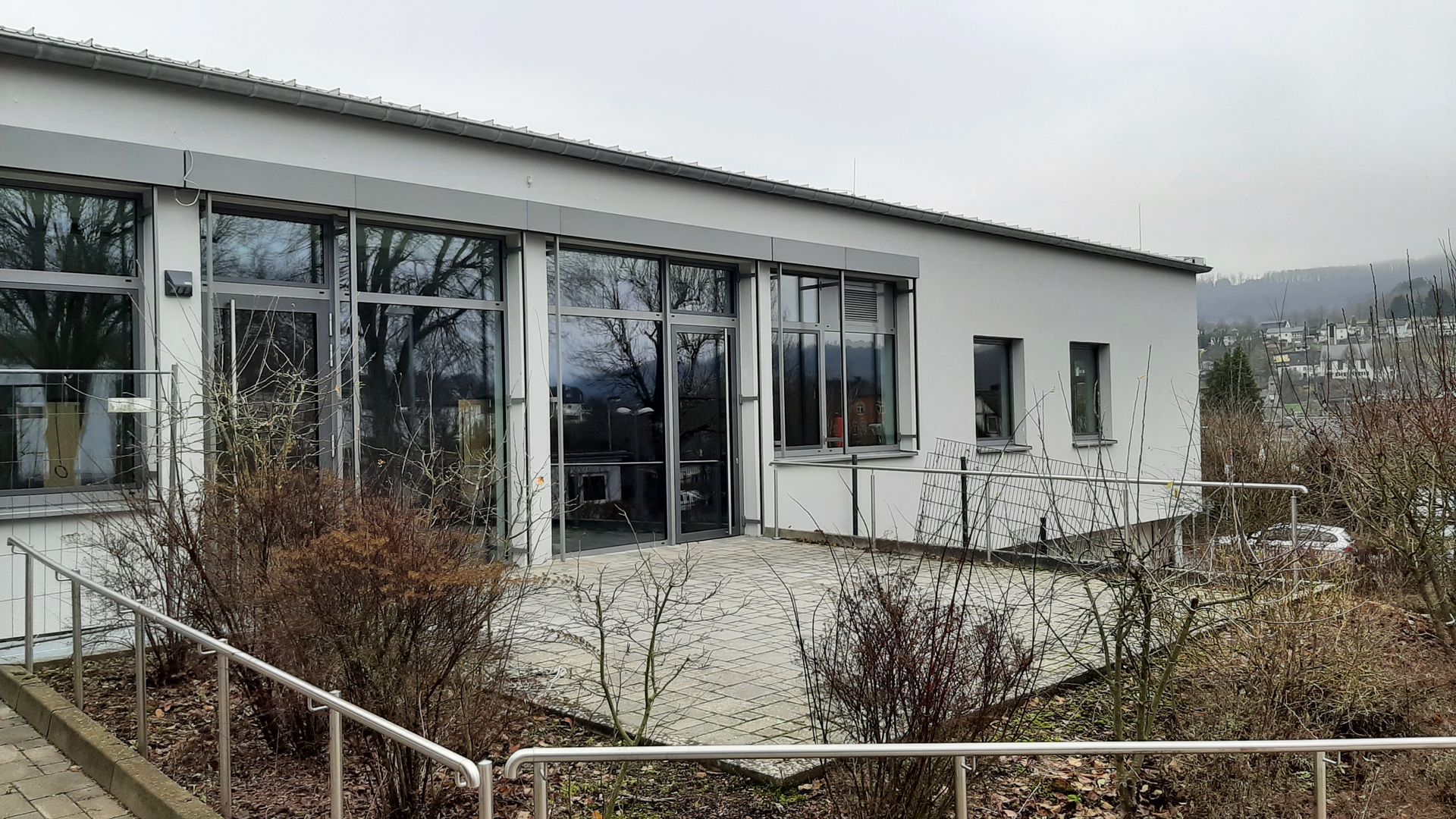 Ein eingeschossiges weißes Gebäude mit großer Glasfassade, gepflastertem Innenhof 