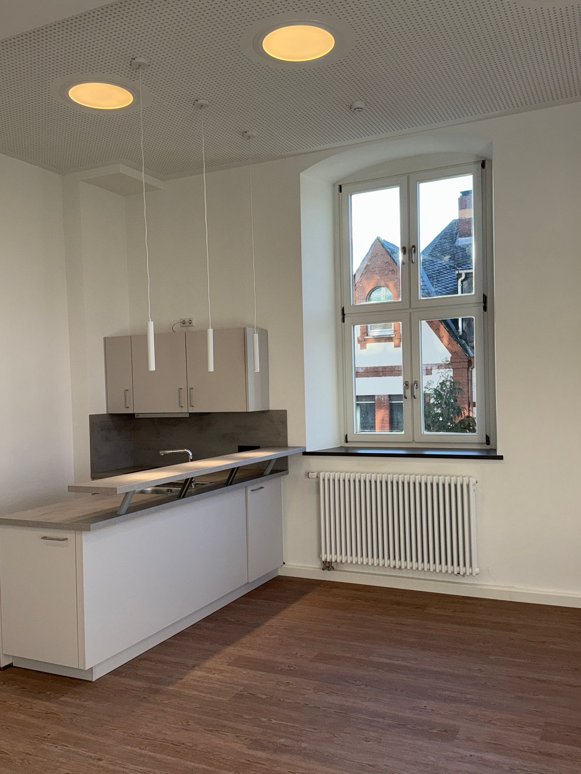 Ein moderner, minimalistischer Küchenbereich mit weißen Schränken, Holzbodenoptik, einem großen Fenster 