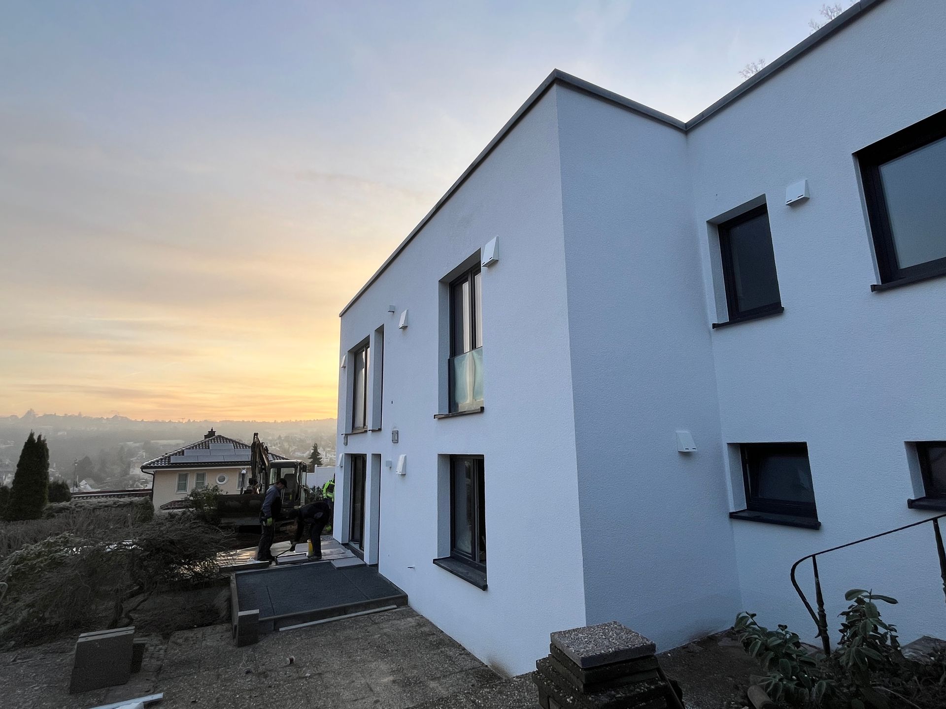 Modernes weißes Haus mit schwarz umrandeten Fenstern vor einem Sonnenuntergangshimmel.