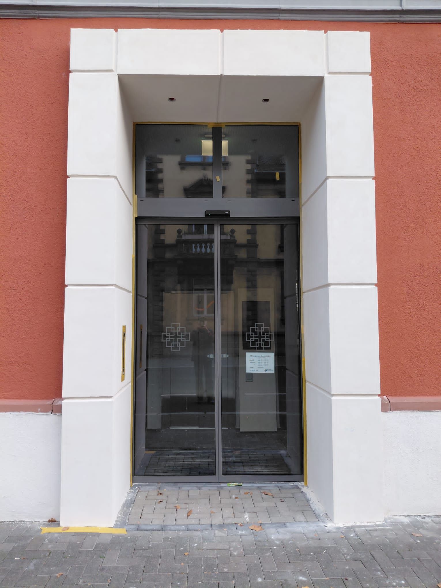 Eine Glasschiebetür in einem weißen Steinportal vor einer roten Gebäudewand.