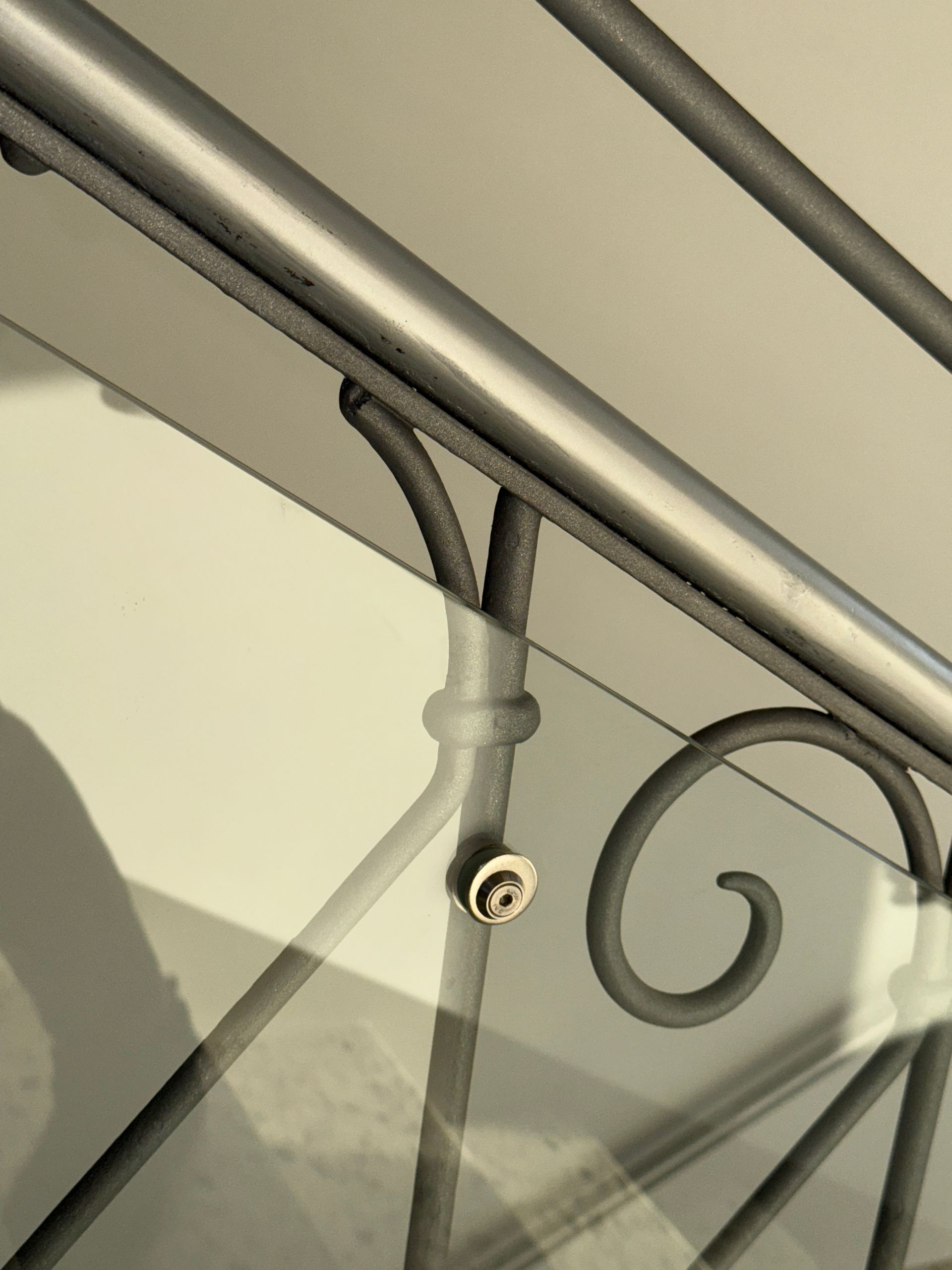 Nahaufnahme eines Metallgeländers mit dekorativen Verzierungen, das mit einem kleinen, runden Befestigungselement 