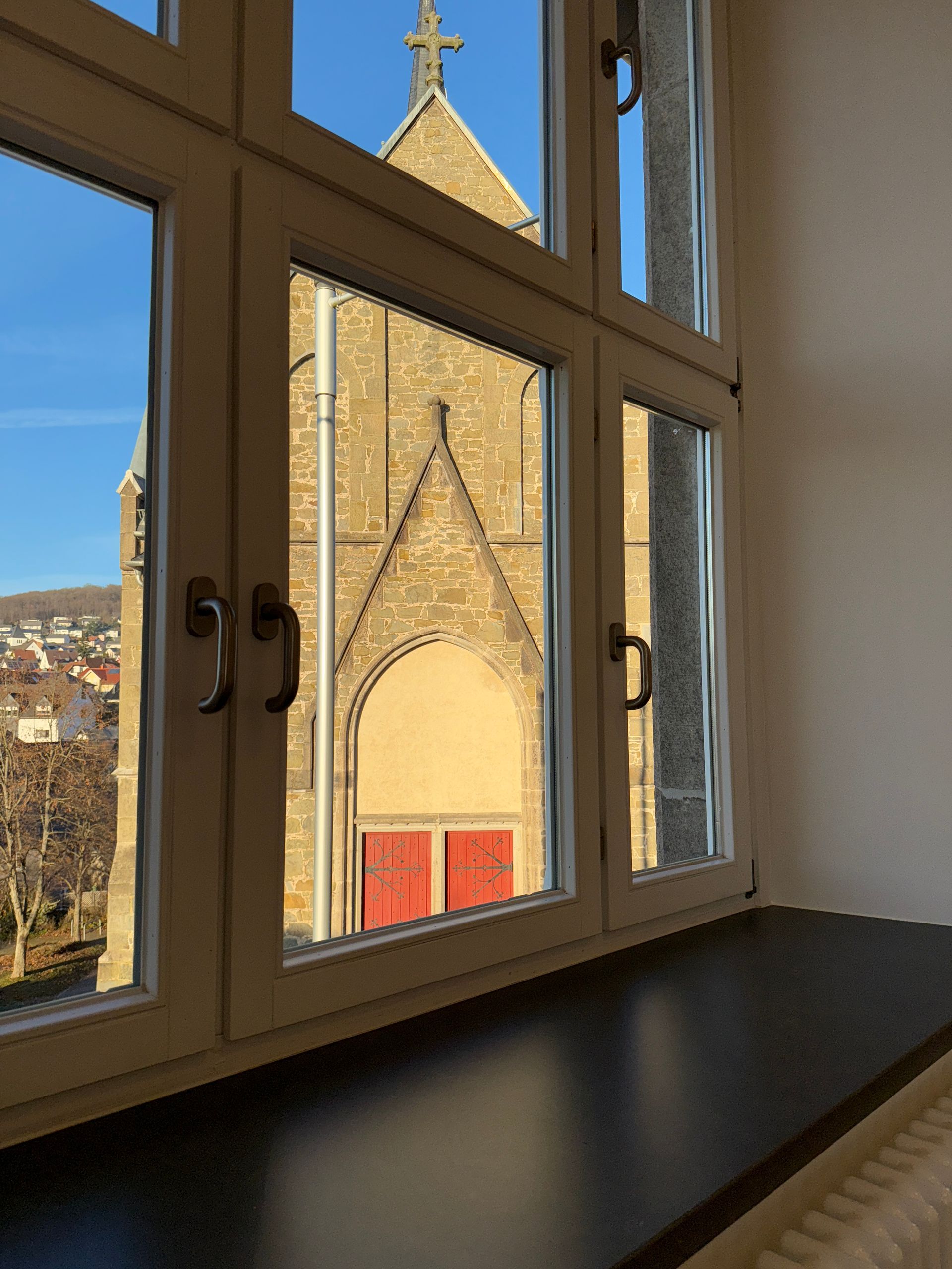 Eine Steinkirche mit roten Türen, gesehen durch ein mehrteiliges Fenster aus einem Innenraum.