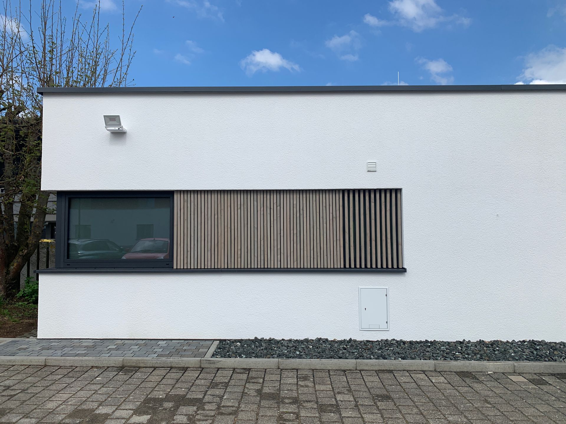 An einer weißen, modernen Gebäudewand befindet sich ein rechteckiges Fenster mit 