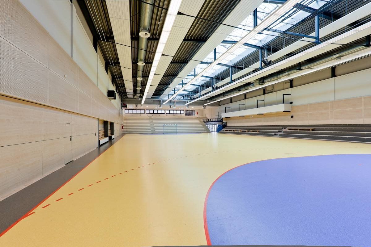 Eine moderne Sporthalle mit hellem Boden, blauen Spielfeldmarkierungen, Holzwänden und einem hohen Oberlicht.