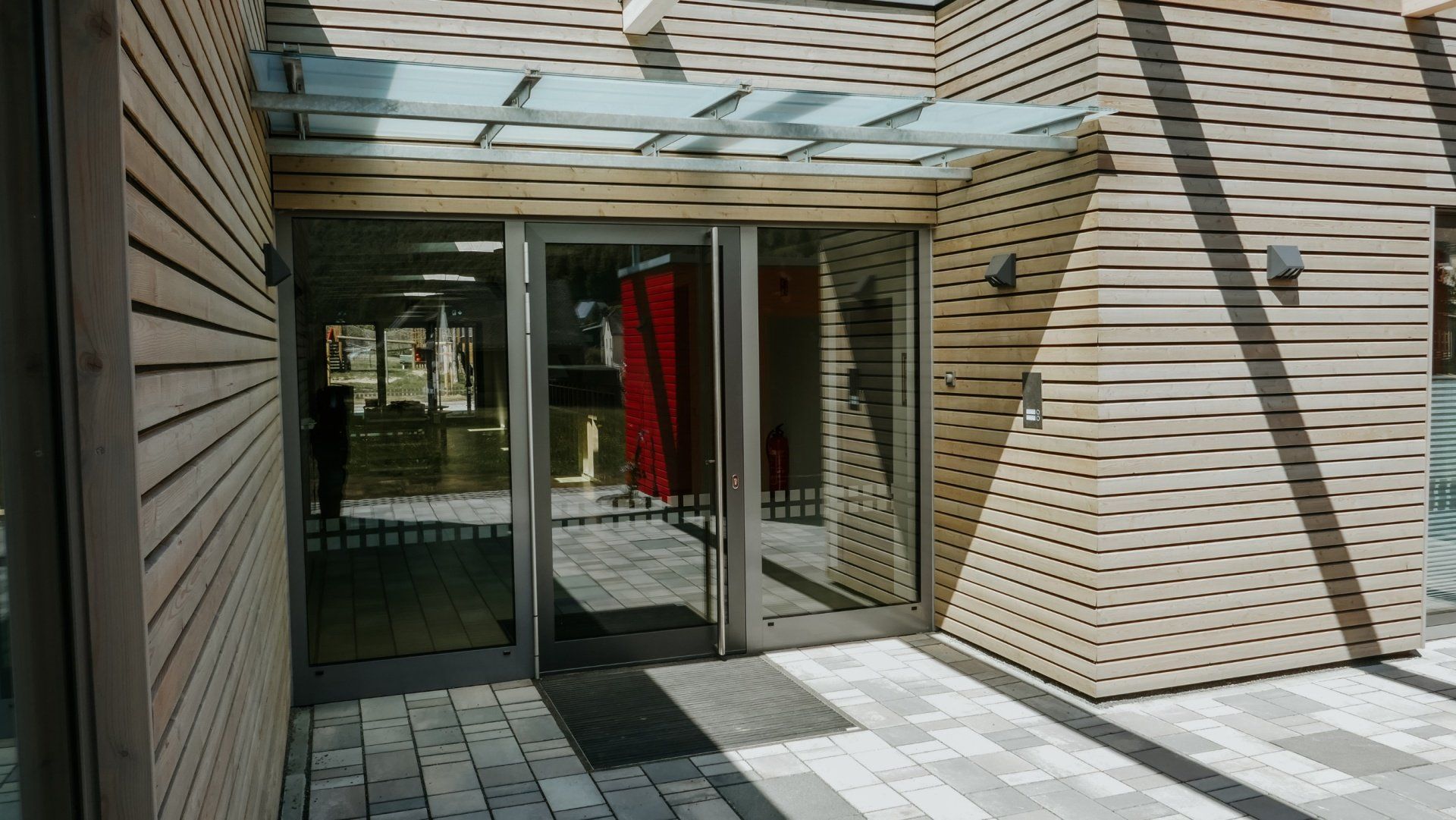 Der Eingang zu einem modernen Gebäude mit horizontaler Holzlamellenverkleidung, einem Glasvordach 