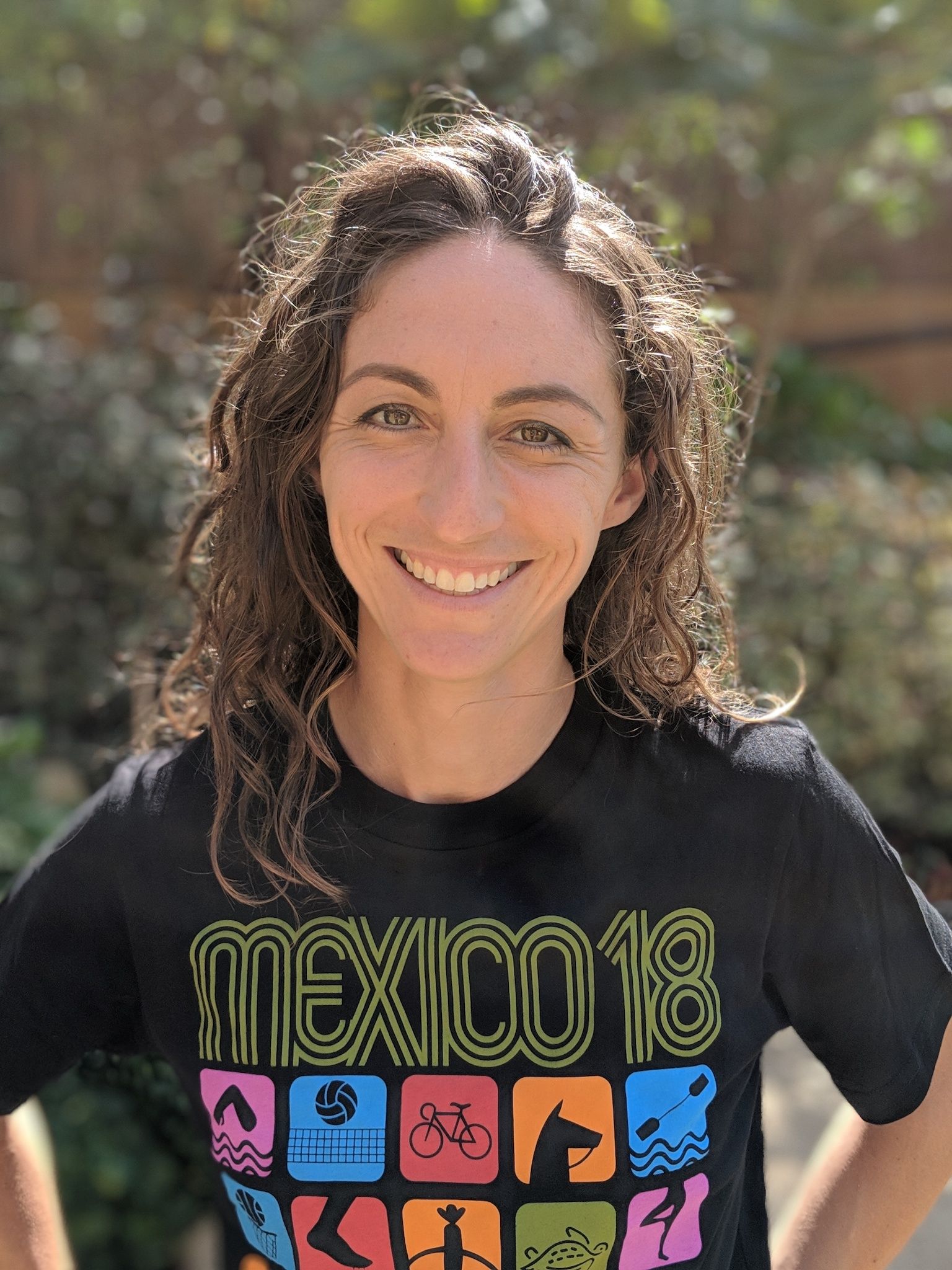 A woman wearing a t-shirt that says mexico 18 is smiling for the camera.