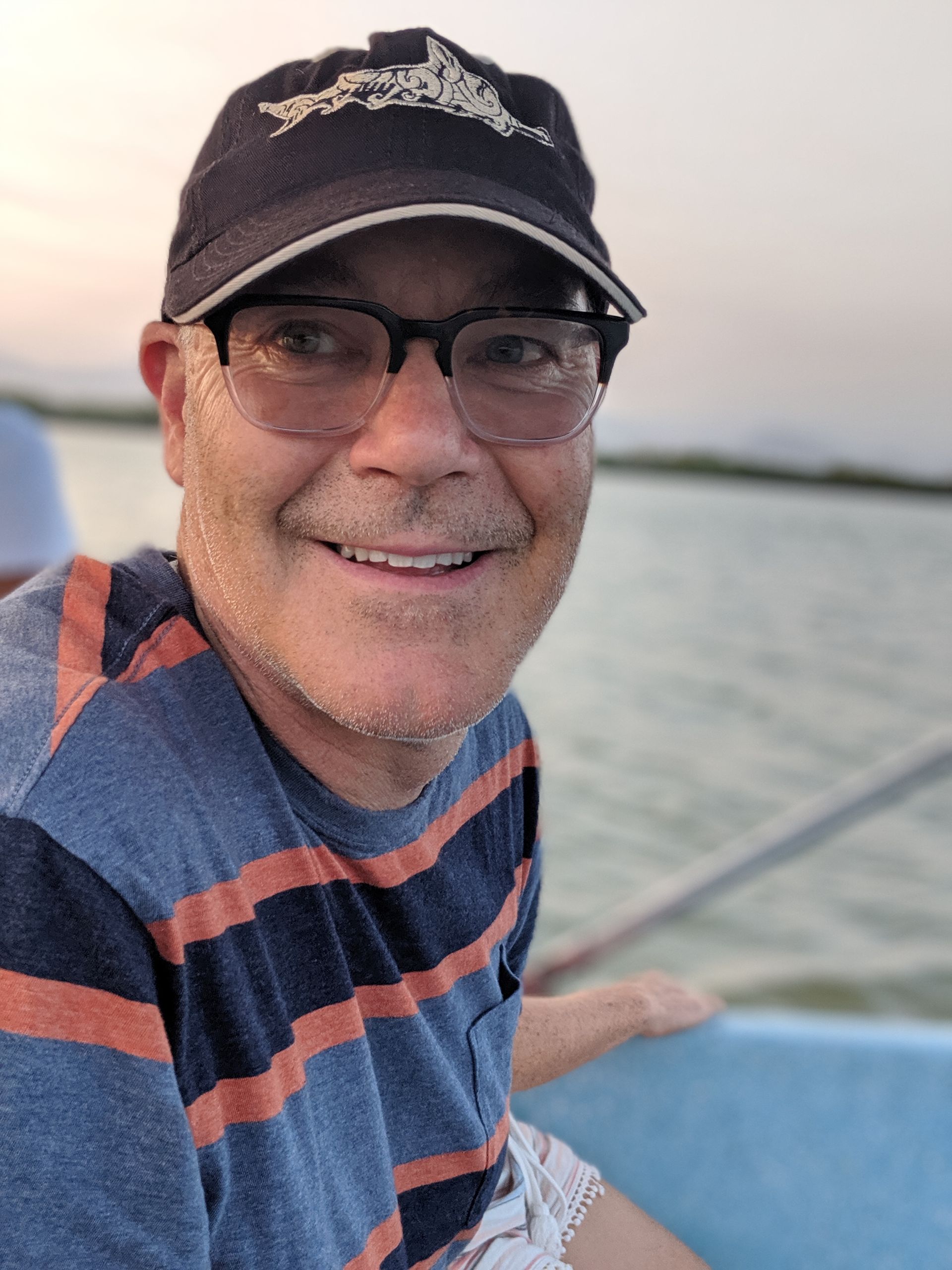 A man wearing a hat and glasses is smiling while sitting on a boat.