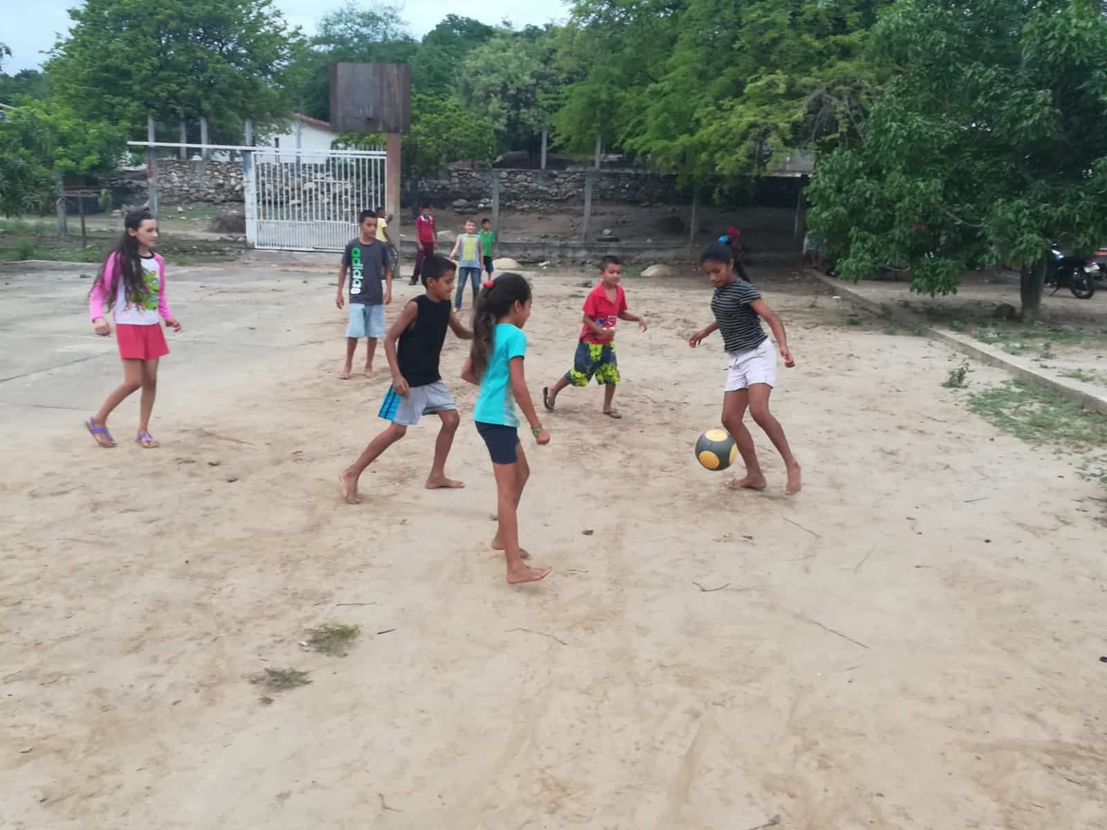 A group of children are playing soccer on a dirt field.