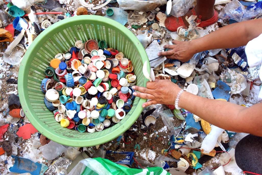 A person is holding a green basket filled with plastic bottle caps.