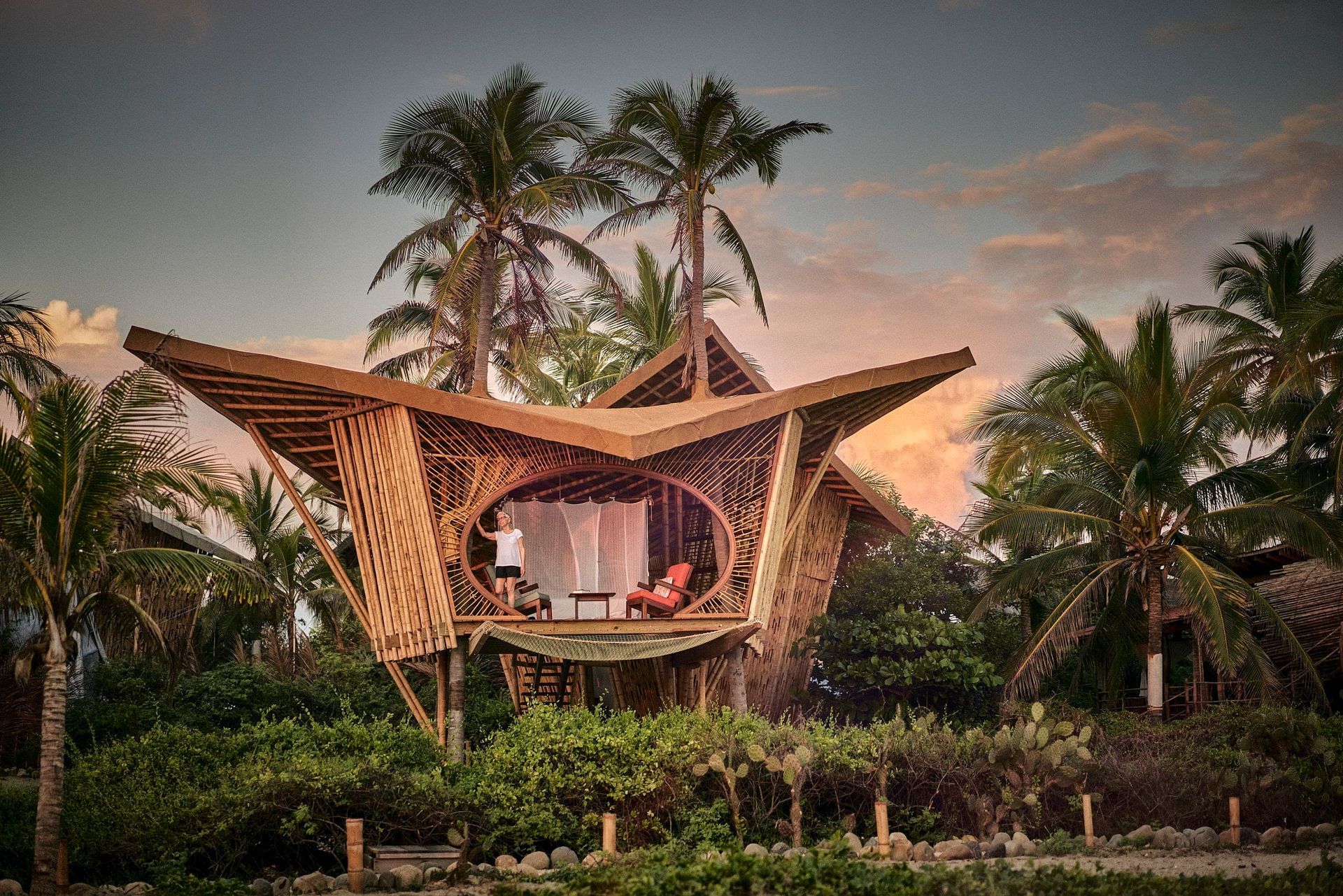 A bamboo house surrounded by palm trees in the middle of a forest.