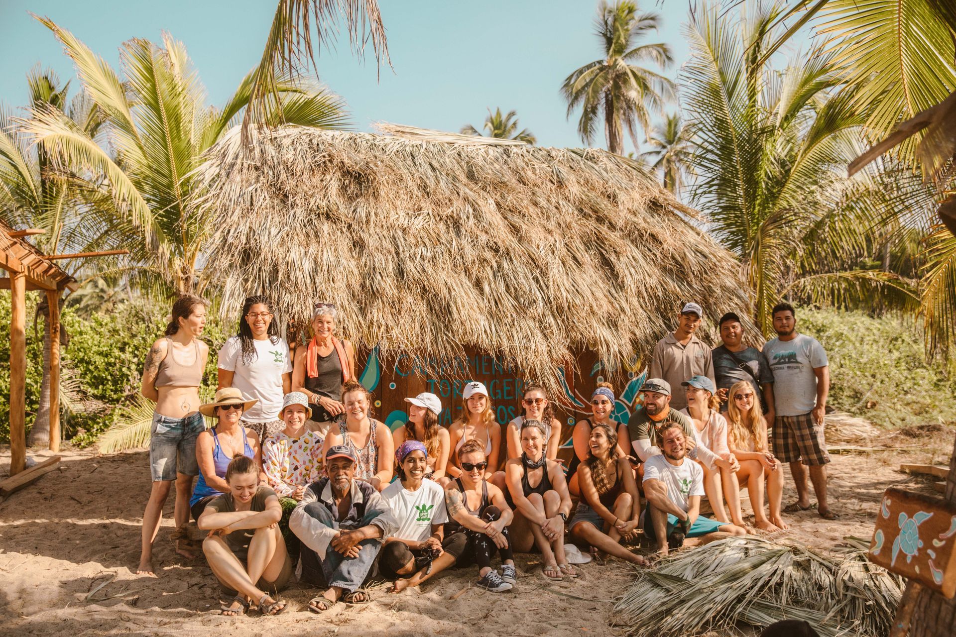 A group of people are posing for a picture in front of a thatched hut.
