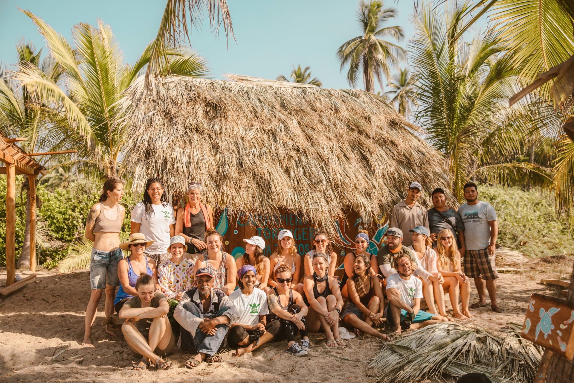 A group of people are posing for a picture in front of a thatched hut.