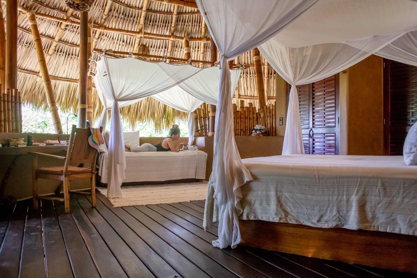 A woman is laying on a canopy bed in a hotel room.