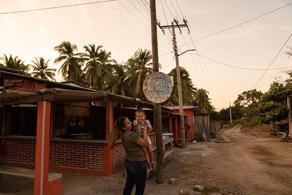 A woman is holding a baby in her arms in front of a sign that says ' mexico ' on it