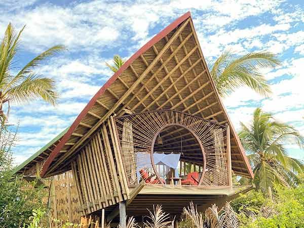 A wooden house with a triangle shaped roof is surrounded by palm trees.