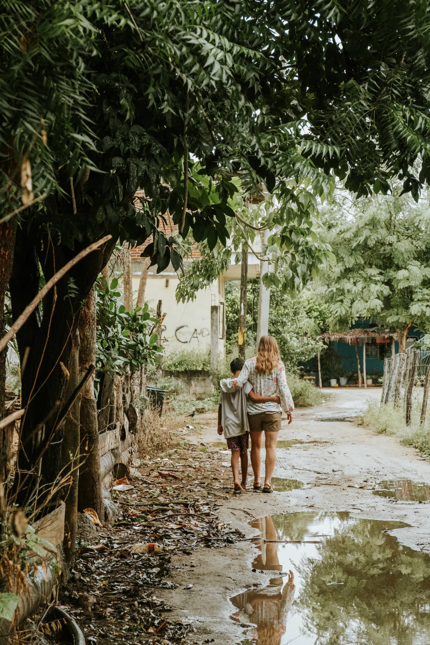A woman and a child are walking down a muddy path.