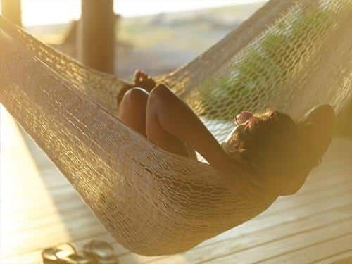 A woman is laying in a hammock on a wooden deck.