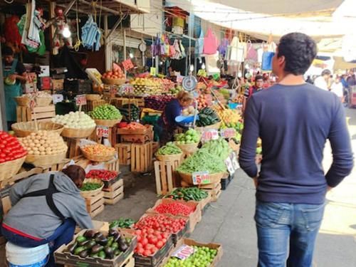 A man is standing in front of a market filled with fruits and vegetables.