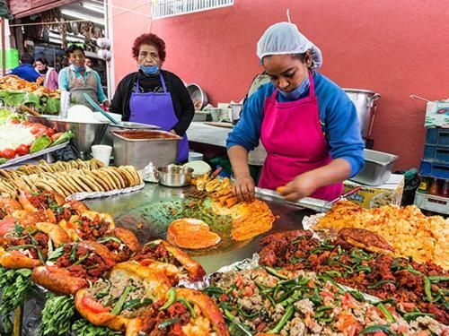 A woman is cooking food on a grill at a market.