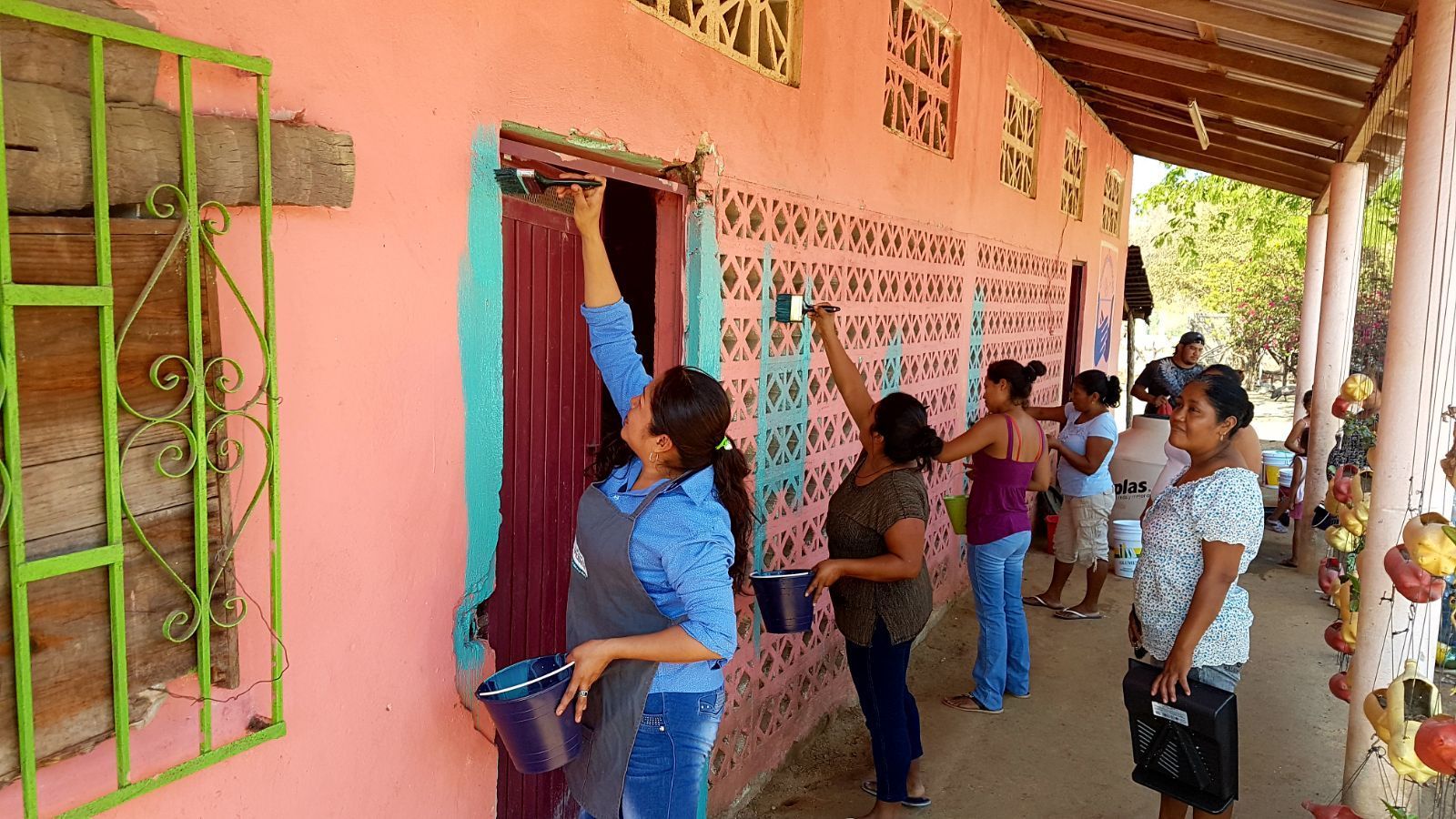 A group of women are painting a pink building.