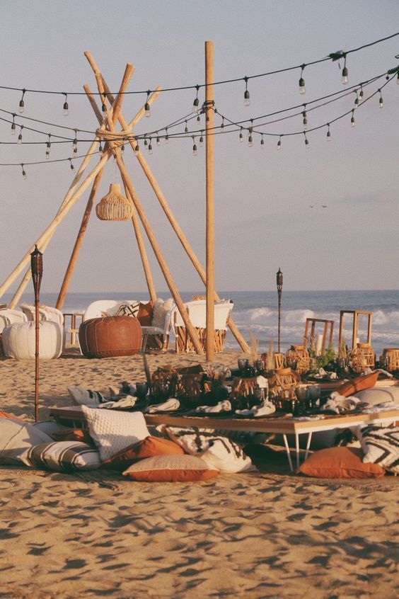There is a teepee on the beach with a table and chairs.