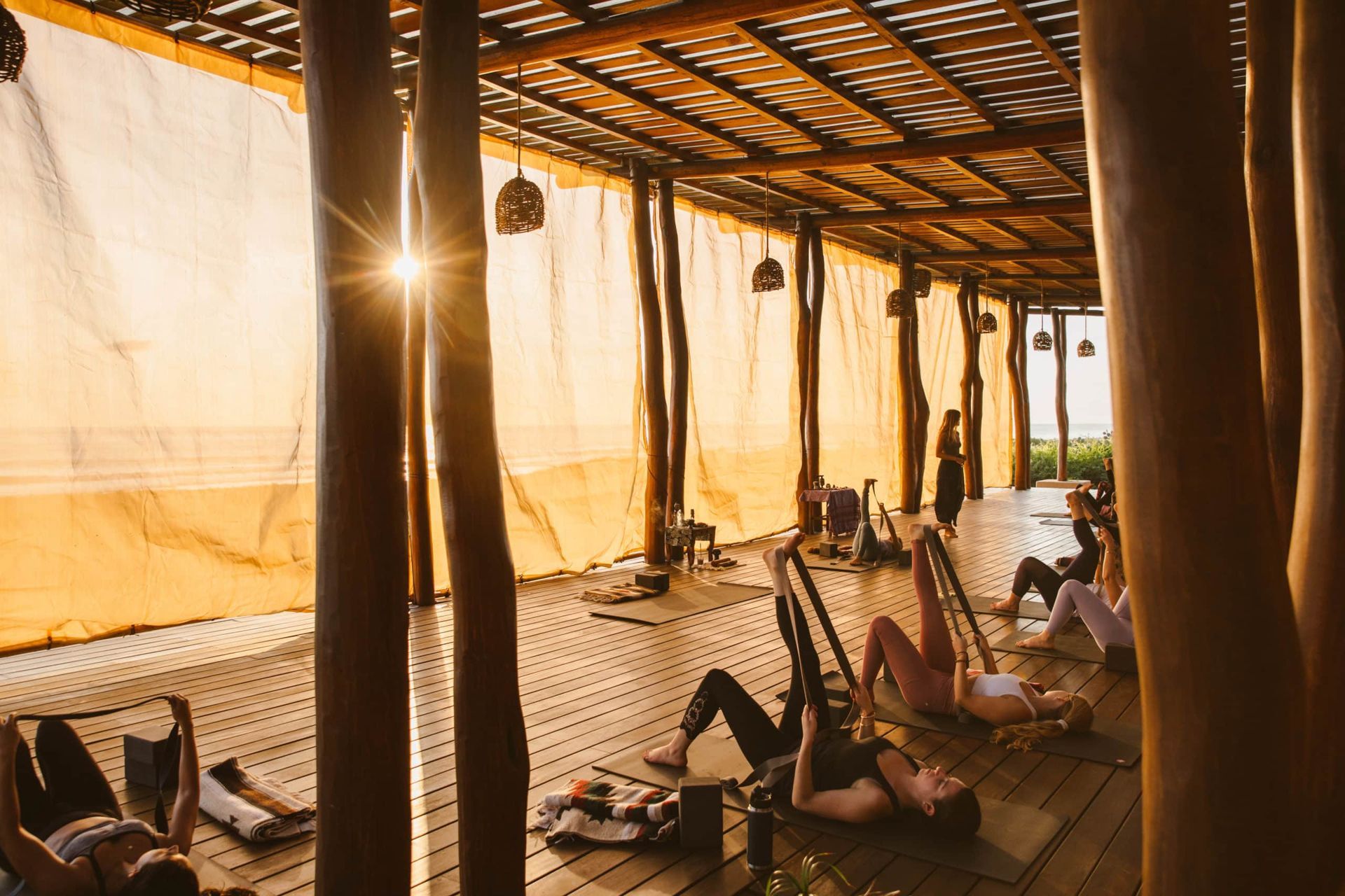 A group of people are doing yoga on a wooden floor under a canopy.