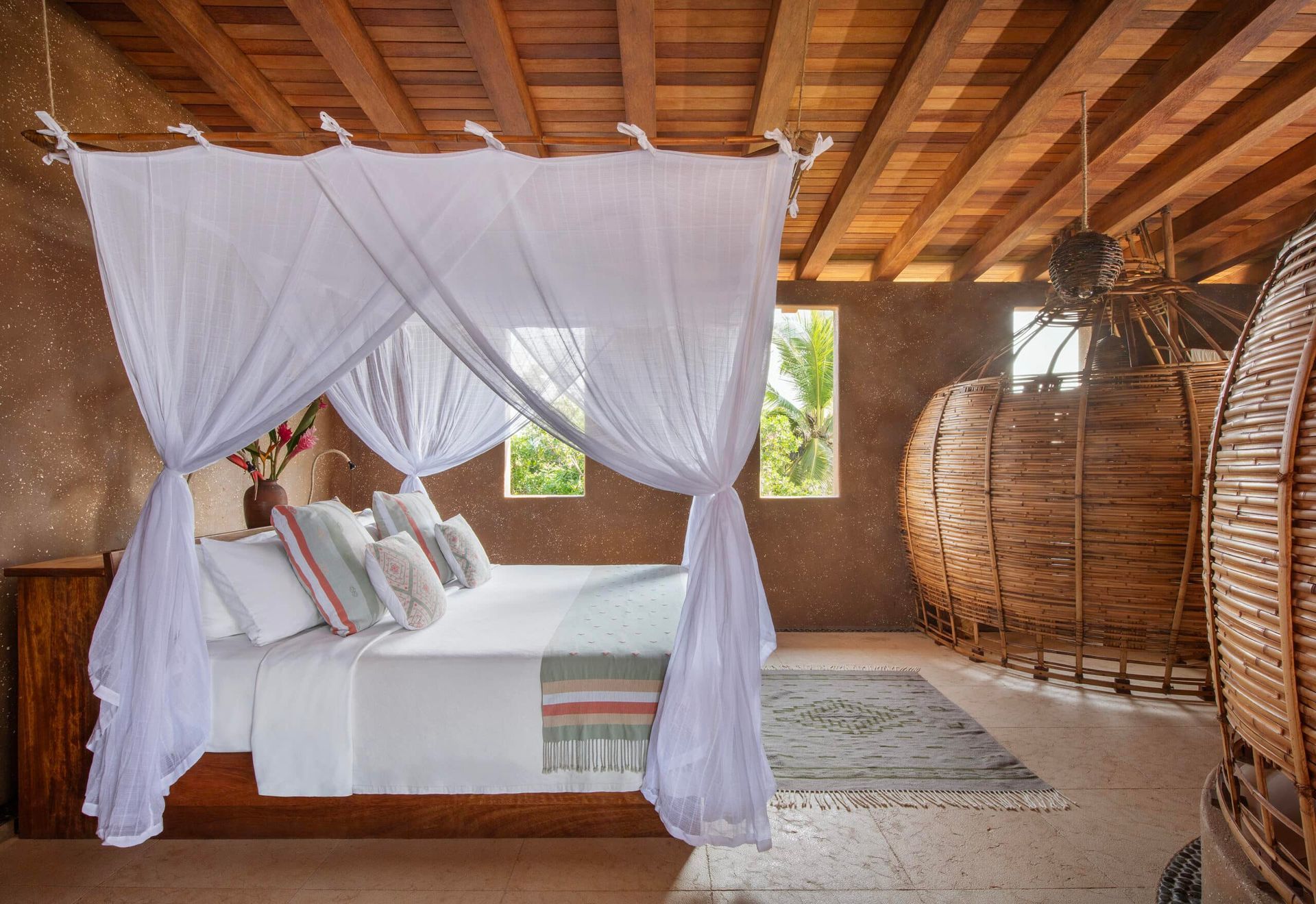 A bedroom with a canopy bed and wicker chairs.