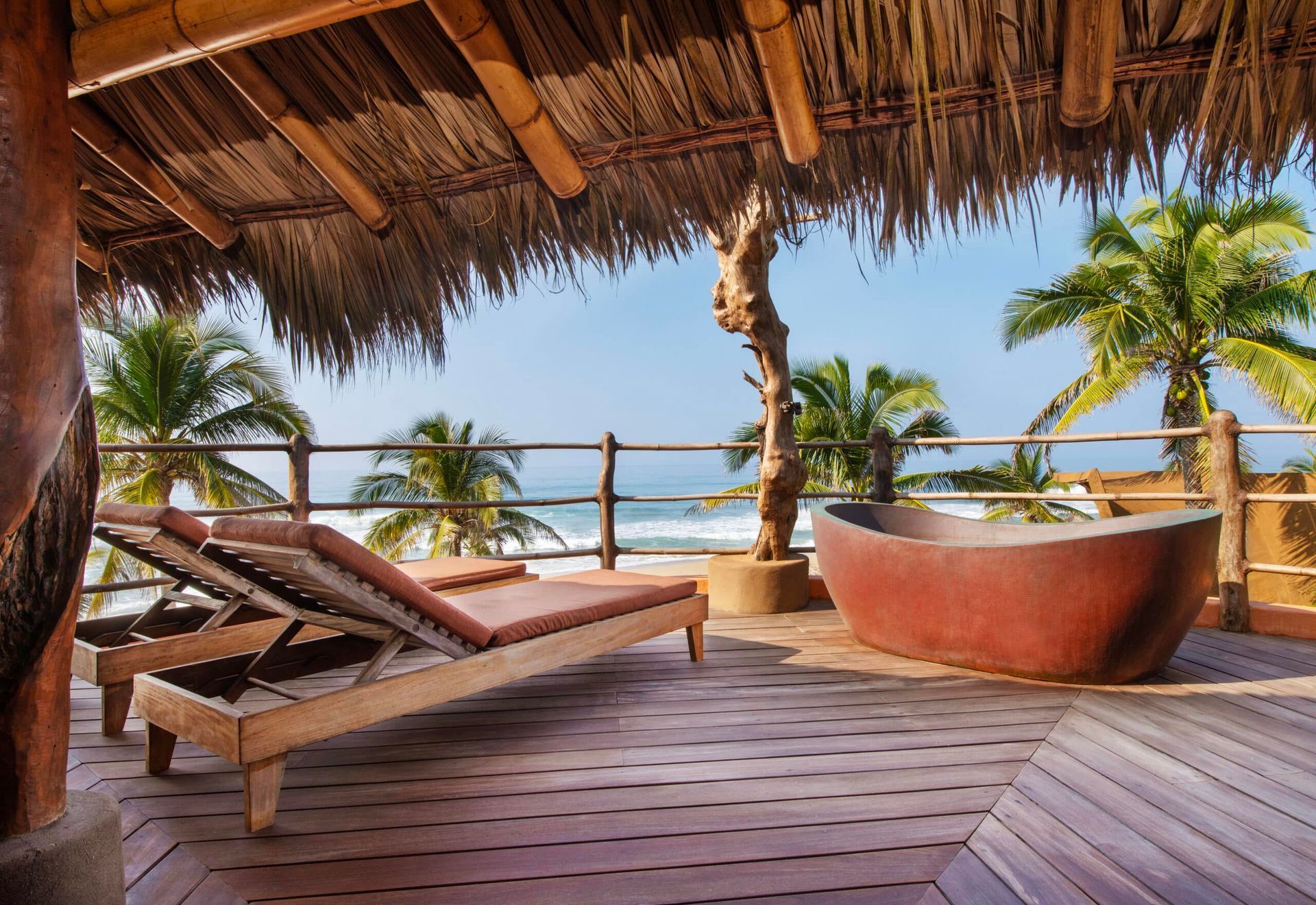 A thatched roof deck with a bathtub and lounge chairs