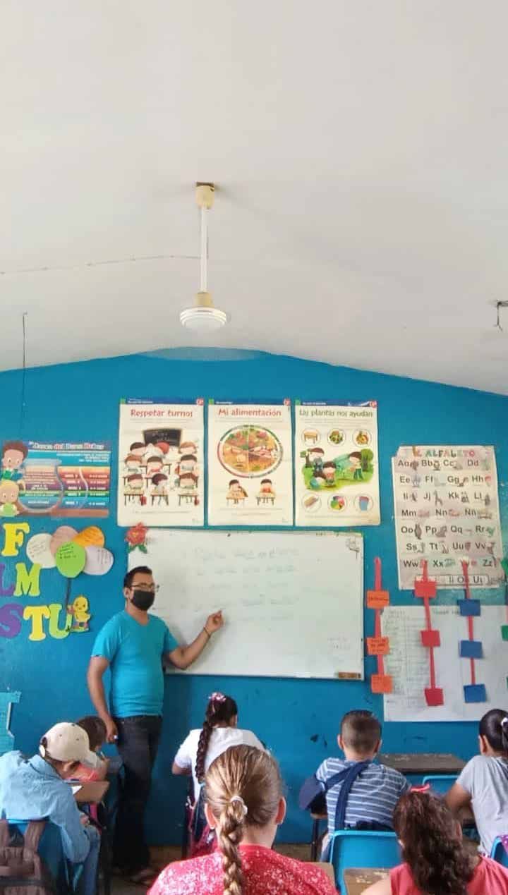 A group of people are sitting in a classroom with a man standing in front of a whiteboard.