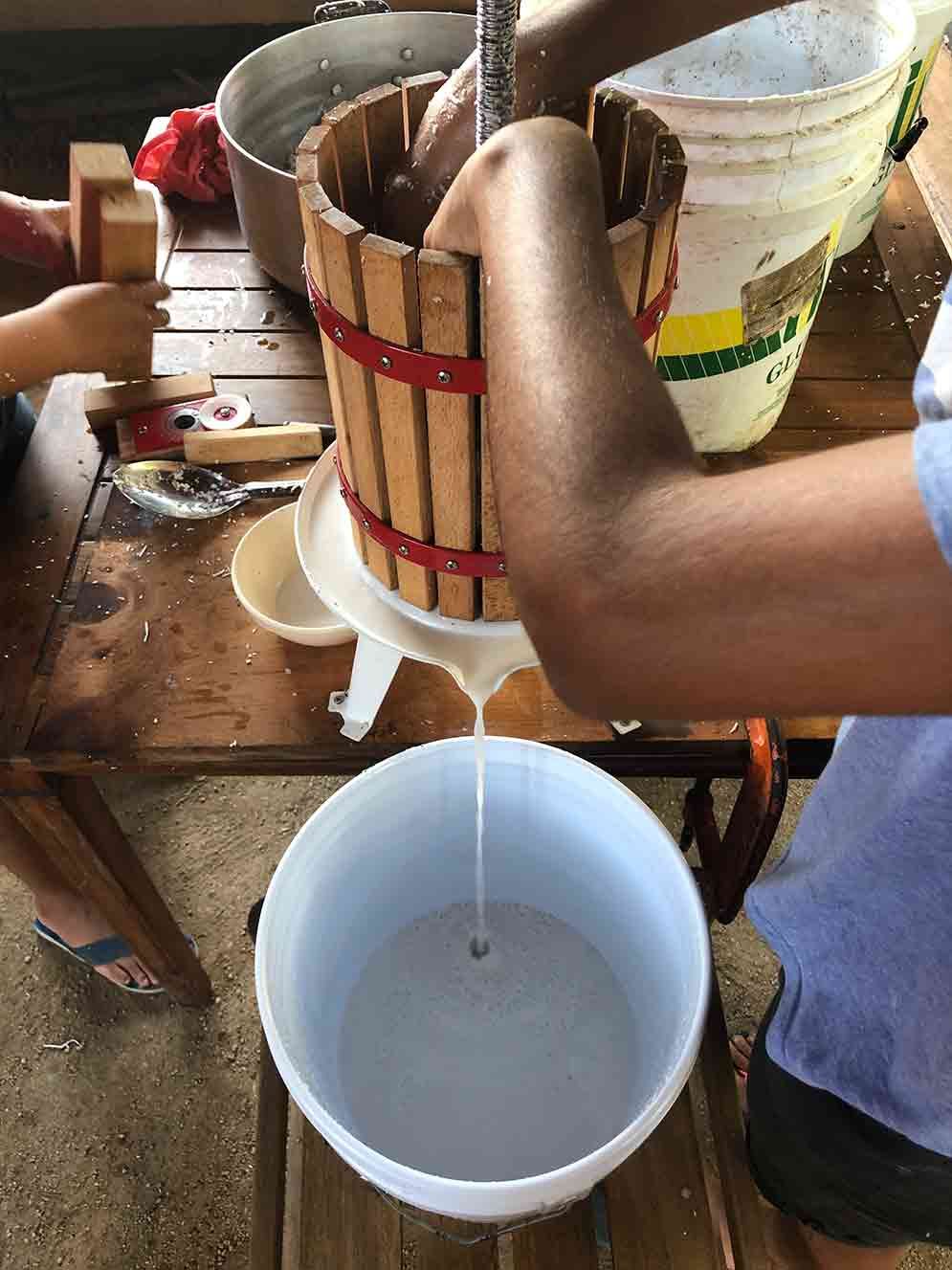 A person is pouring liquid from a wooden bucket into a plastic bucket.