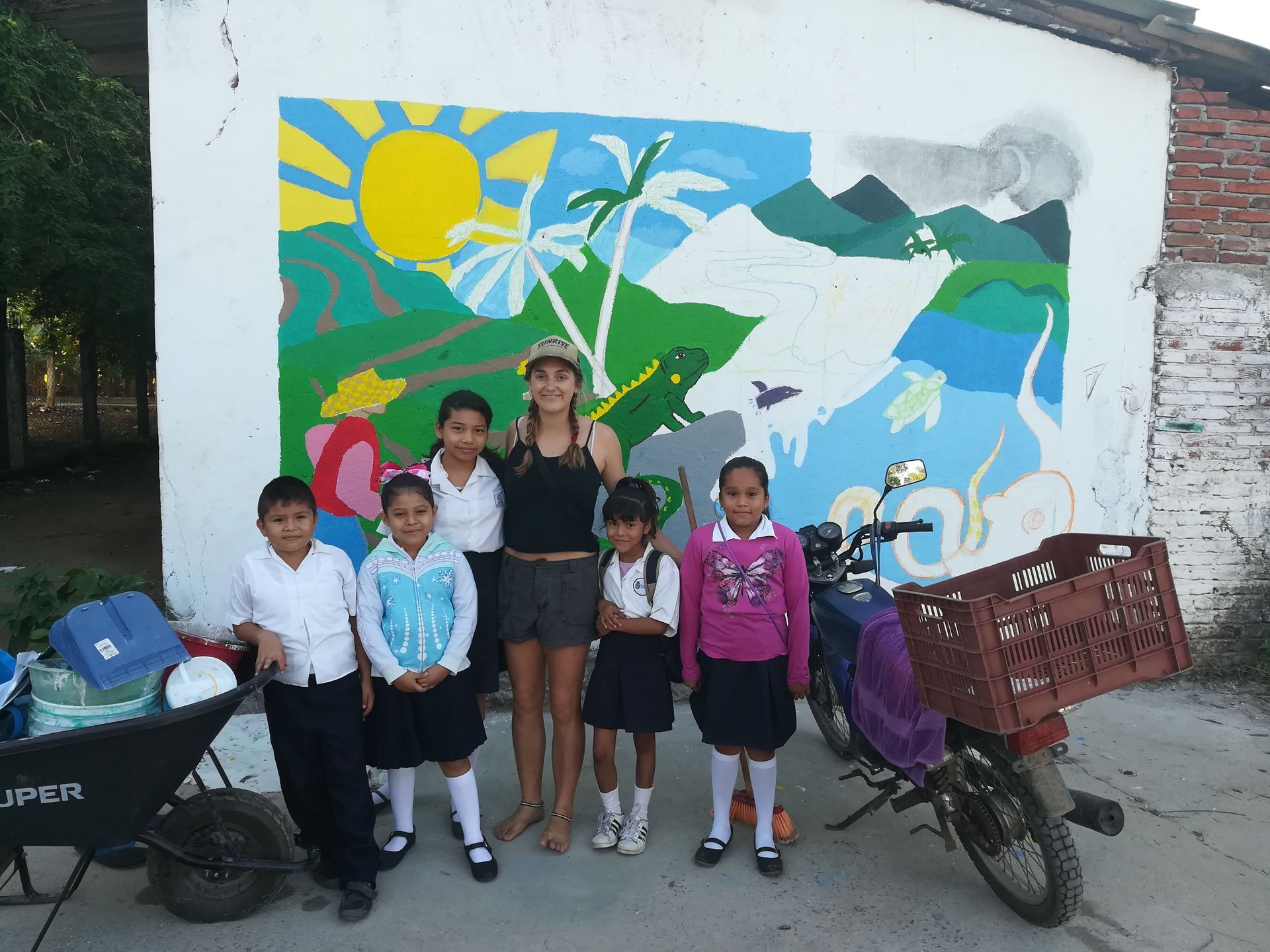 A group of children standing in front of a jeep wheelbarrow