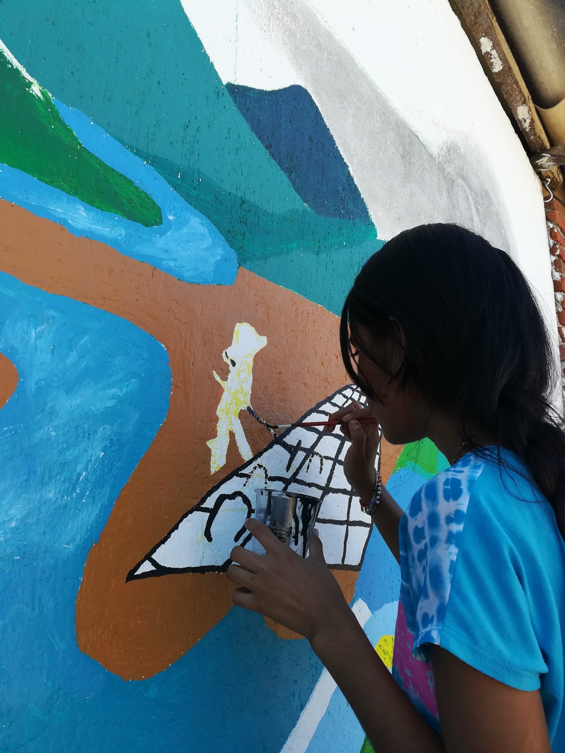 A girl in a blue shirt is painting a picture on a wall