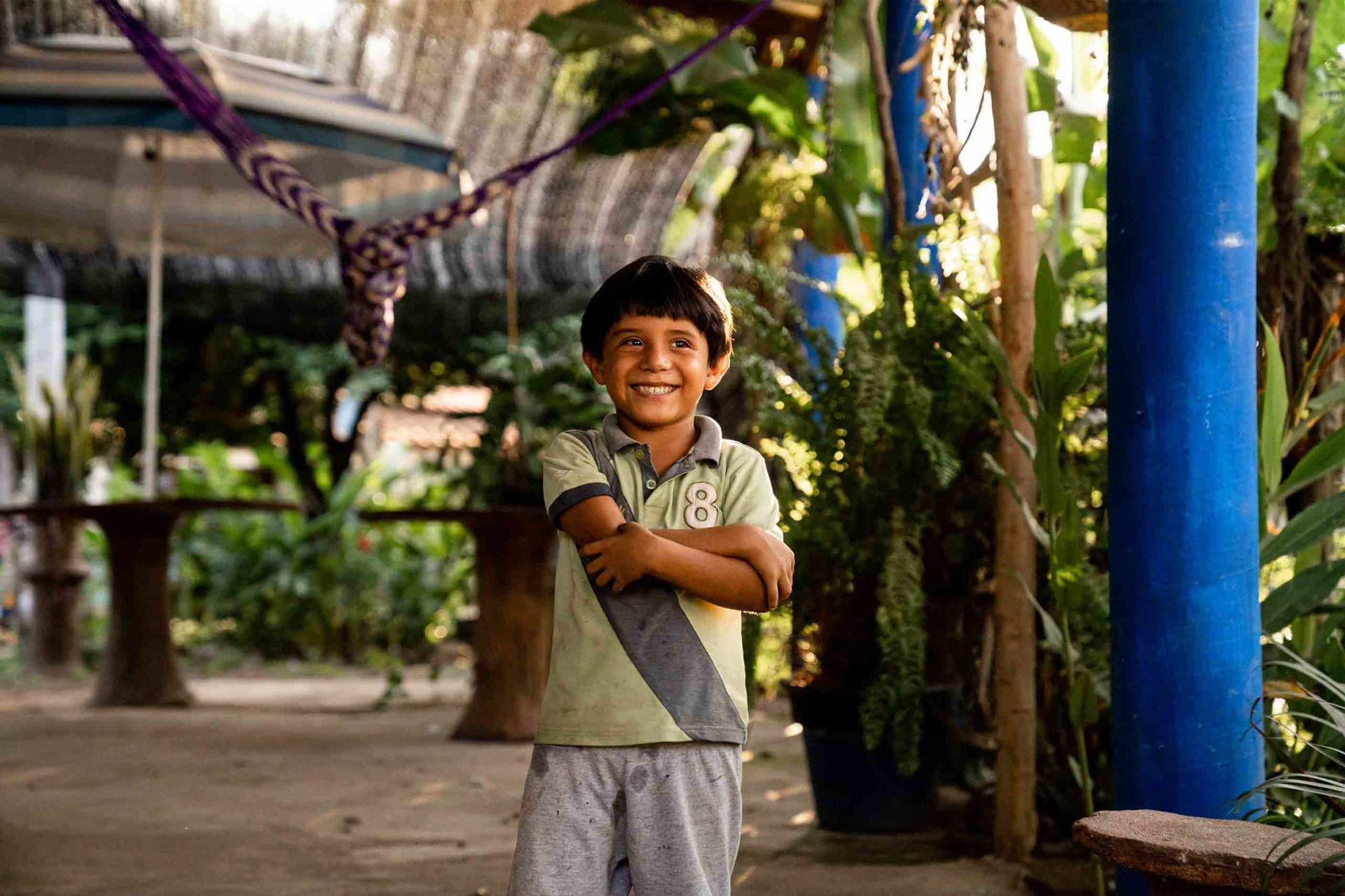 A young boy is standing in front of a blue pole with his arms crossed.