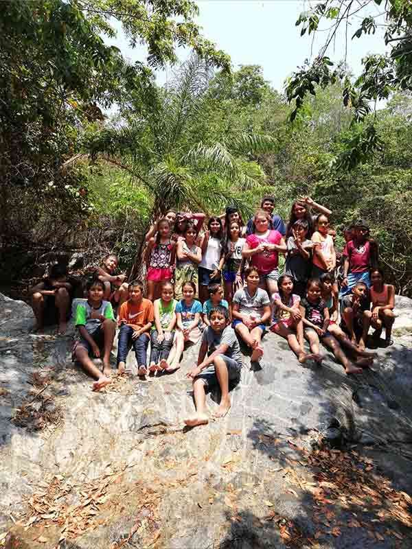 A group of children are sitting on a rock in the woods.