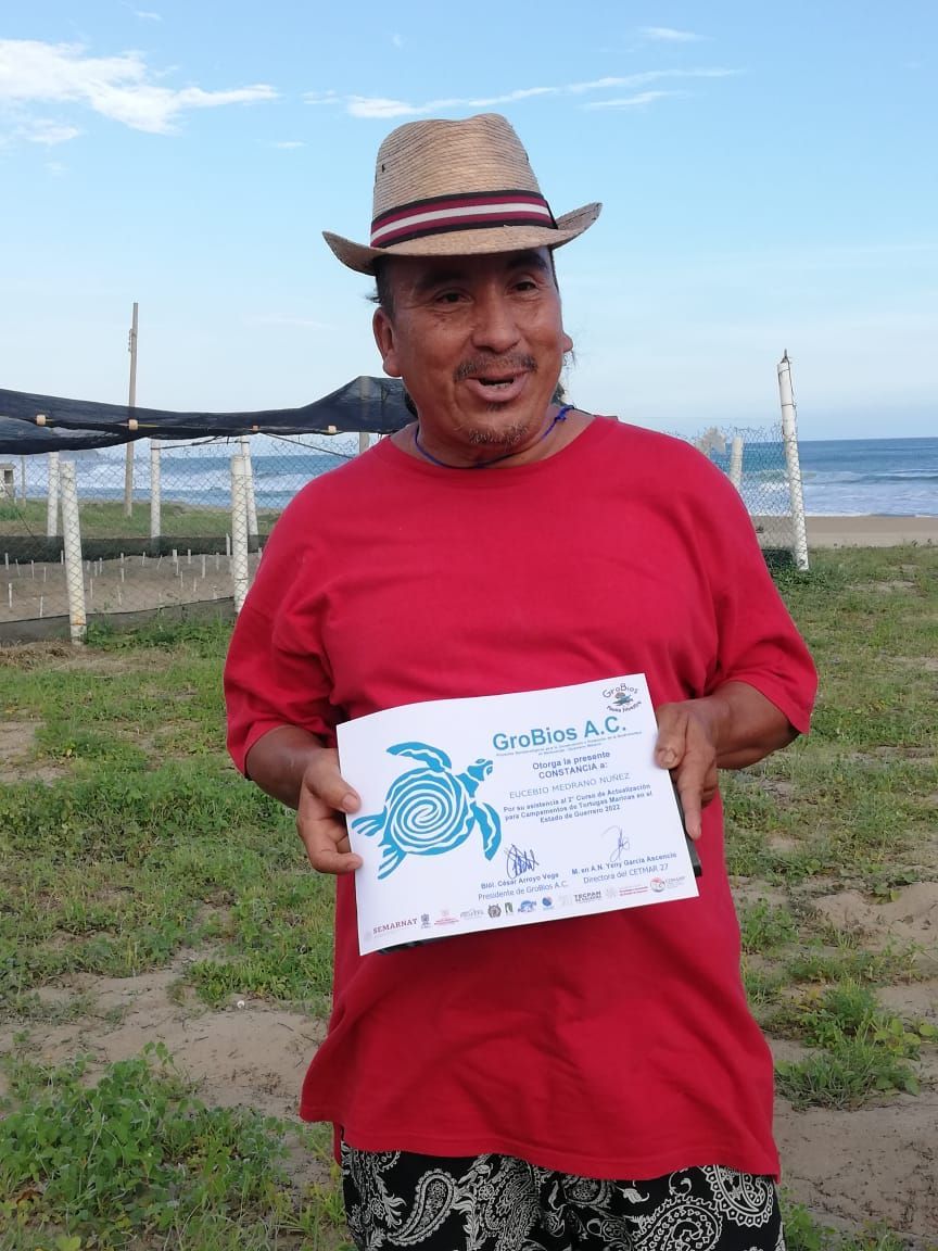A man in a red shirt is holding a sign with a sea turtle on it