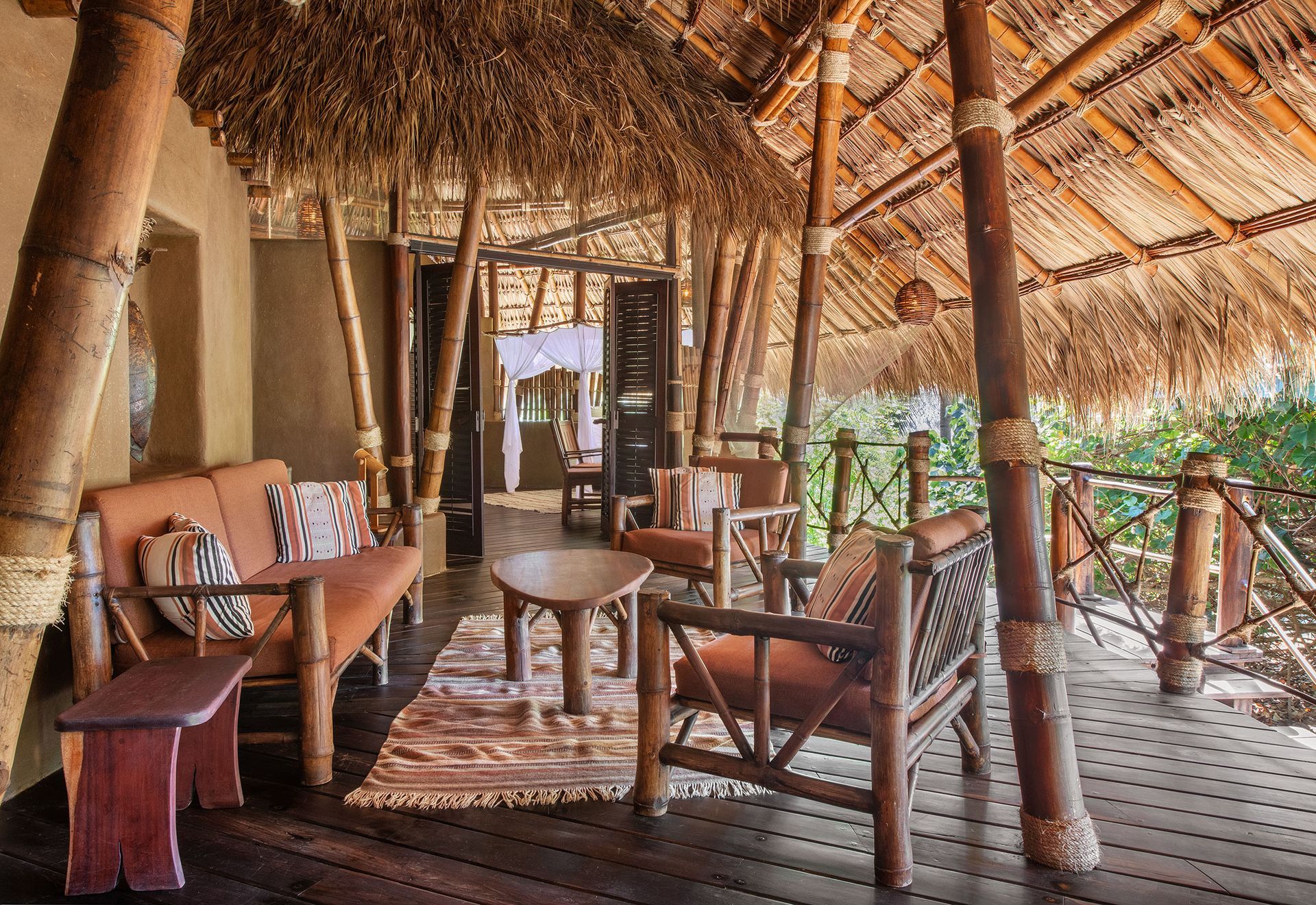 A wooden deck with chairs and a couch under a thatched roof.
