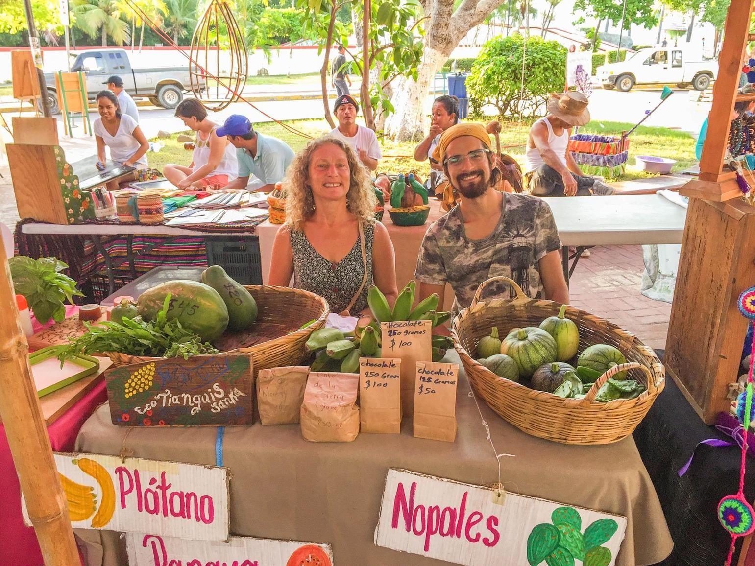 A man and a woman are sitting at a table with baskets of fruit and vegetables.