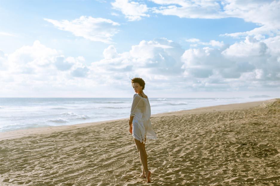 A woman is standing on a sandy beach looking at the ocean.
