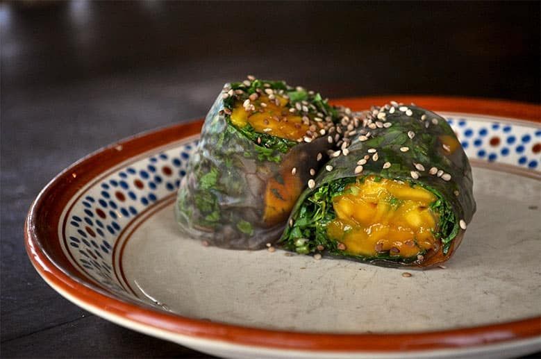 Two vegetable rolls with sesame seeds on a plate on a table.