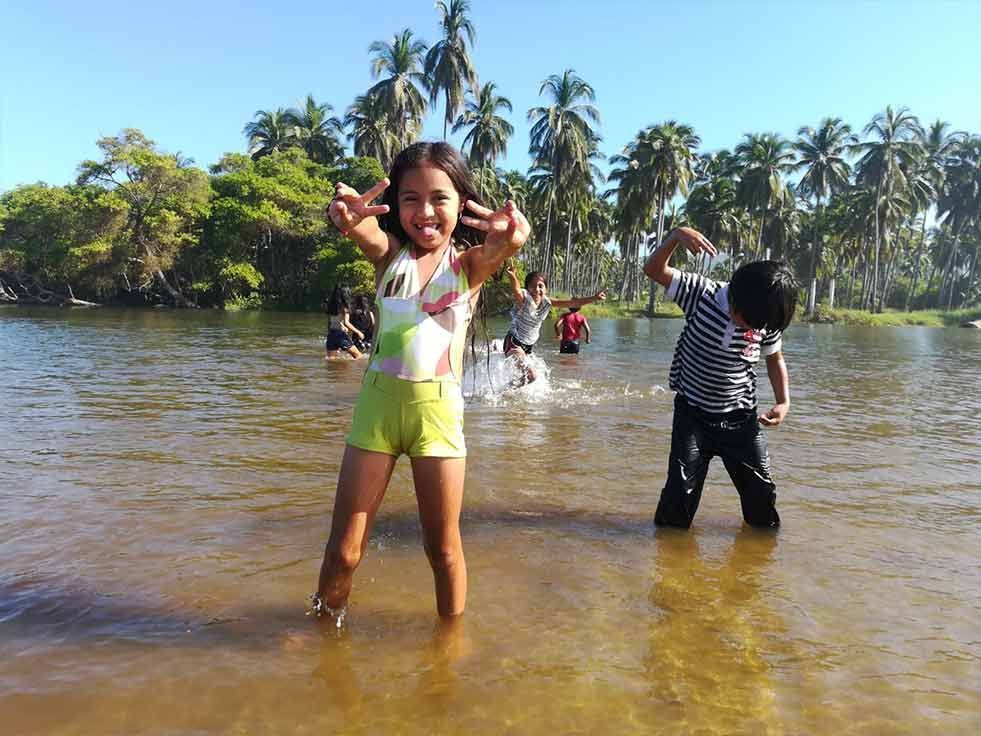 A girl and a boy are standing in the water with palm trees in the background