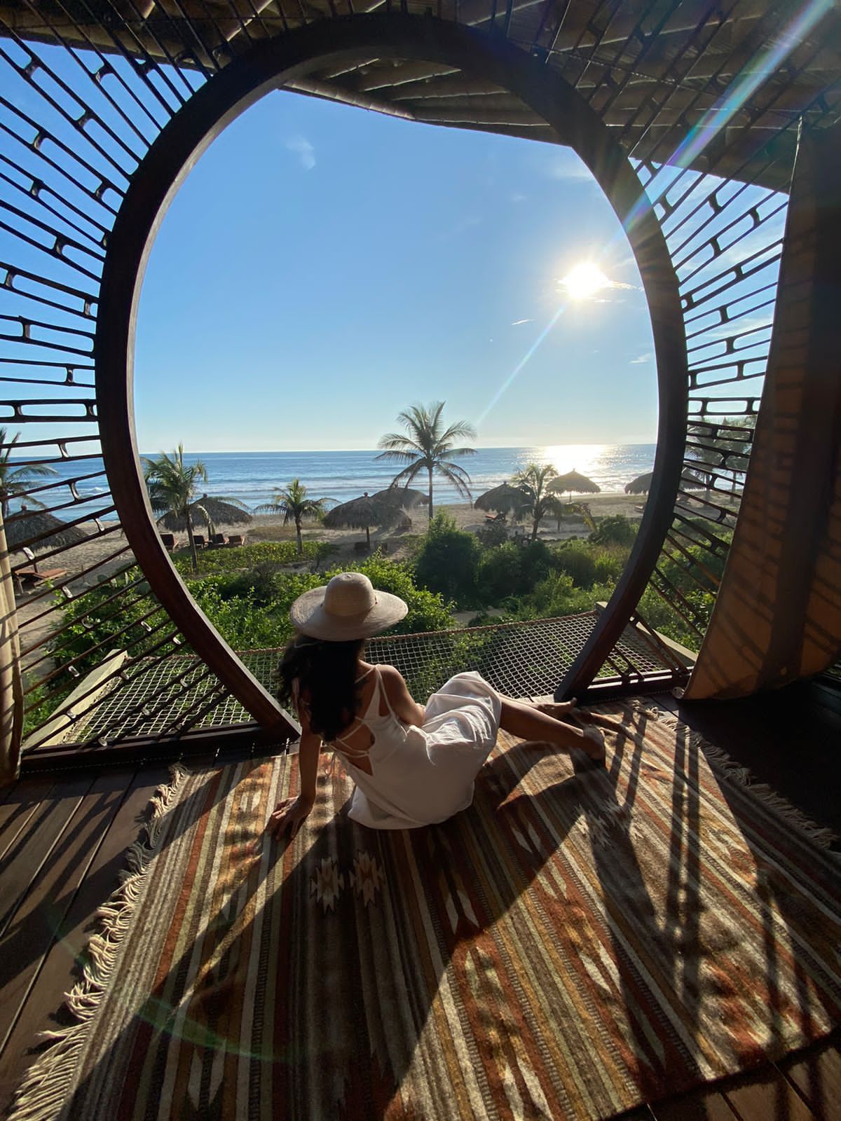 A woman is sitting on a rug in front of a window overlooking the ocean.