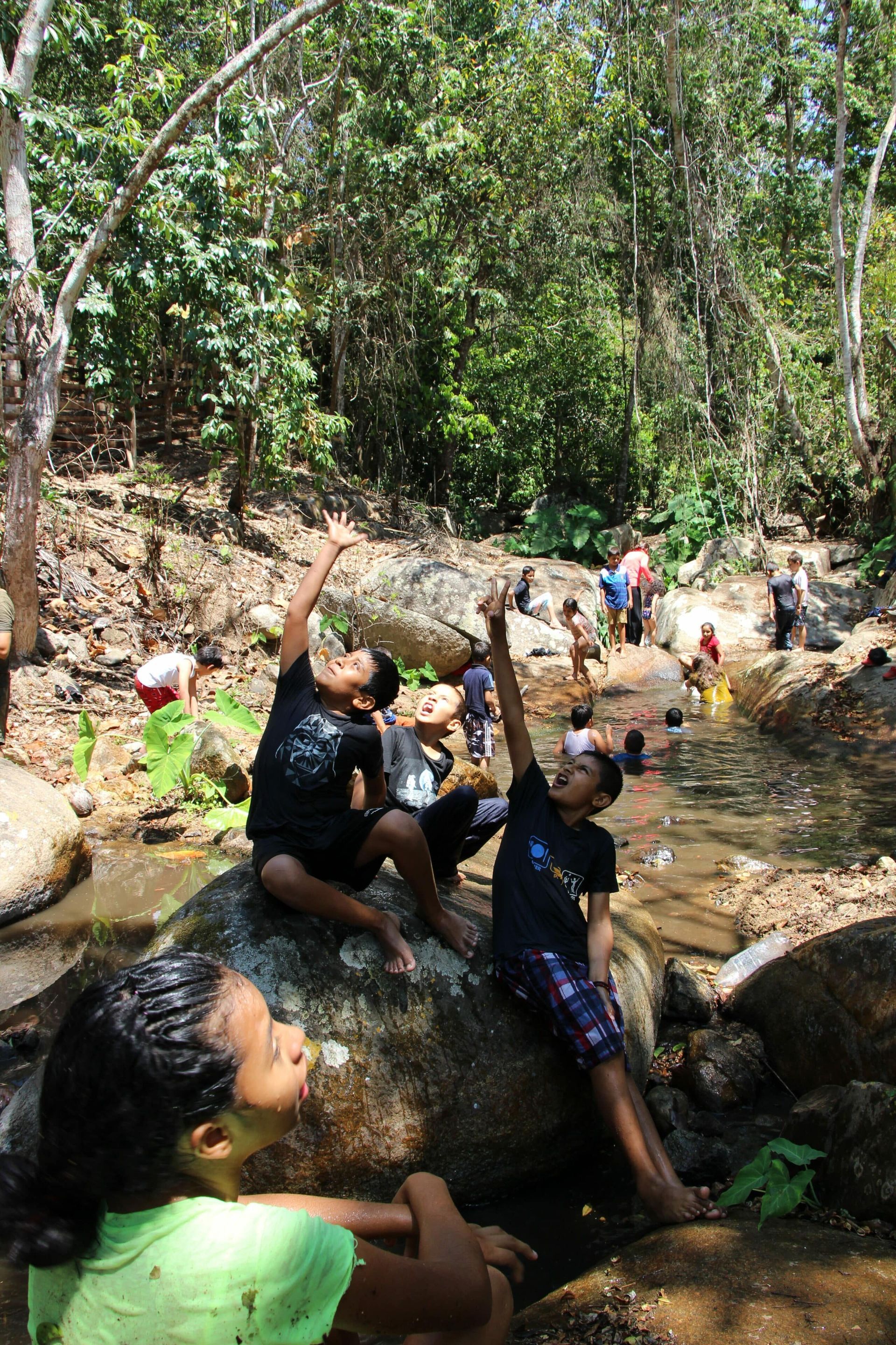 A group of children are sitting on rocks near a river.