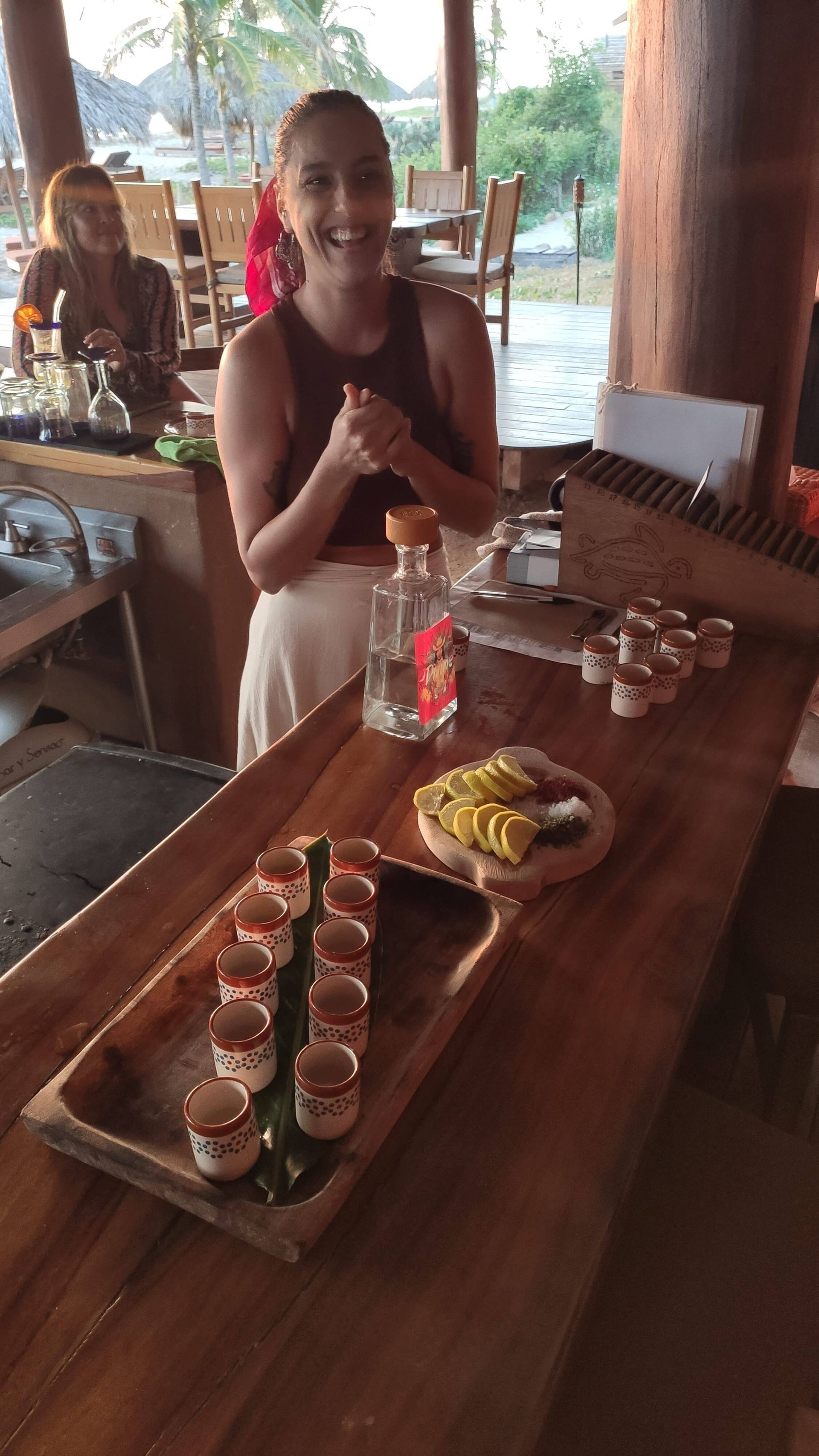 A woman is sitting at a table with a tray of shot glasses on it.