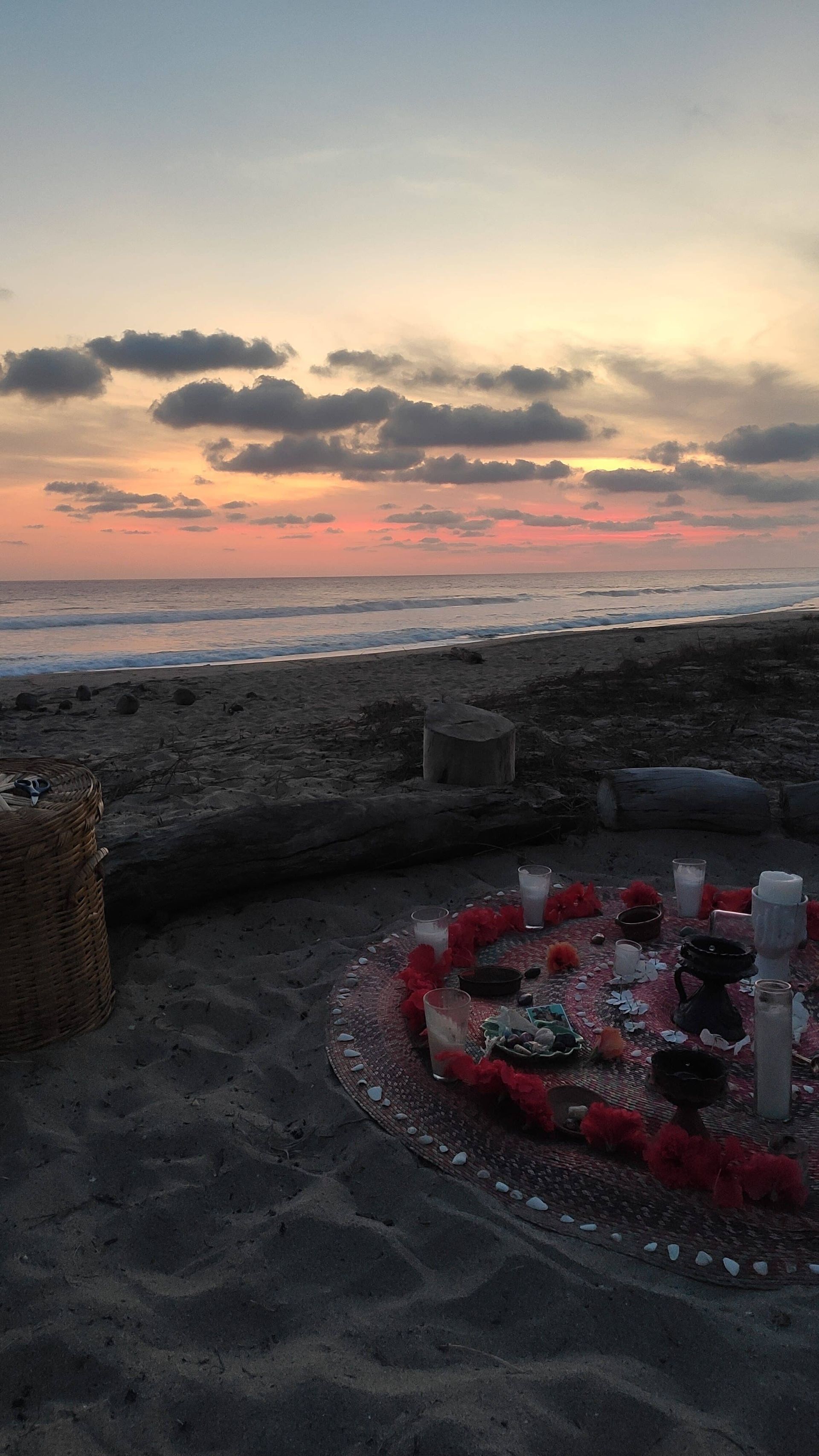 There is a circle of candles on the beach at sunset.