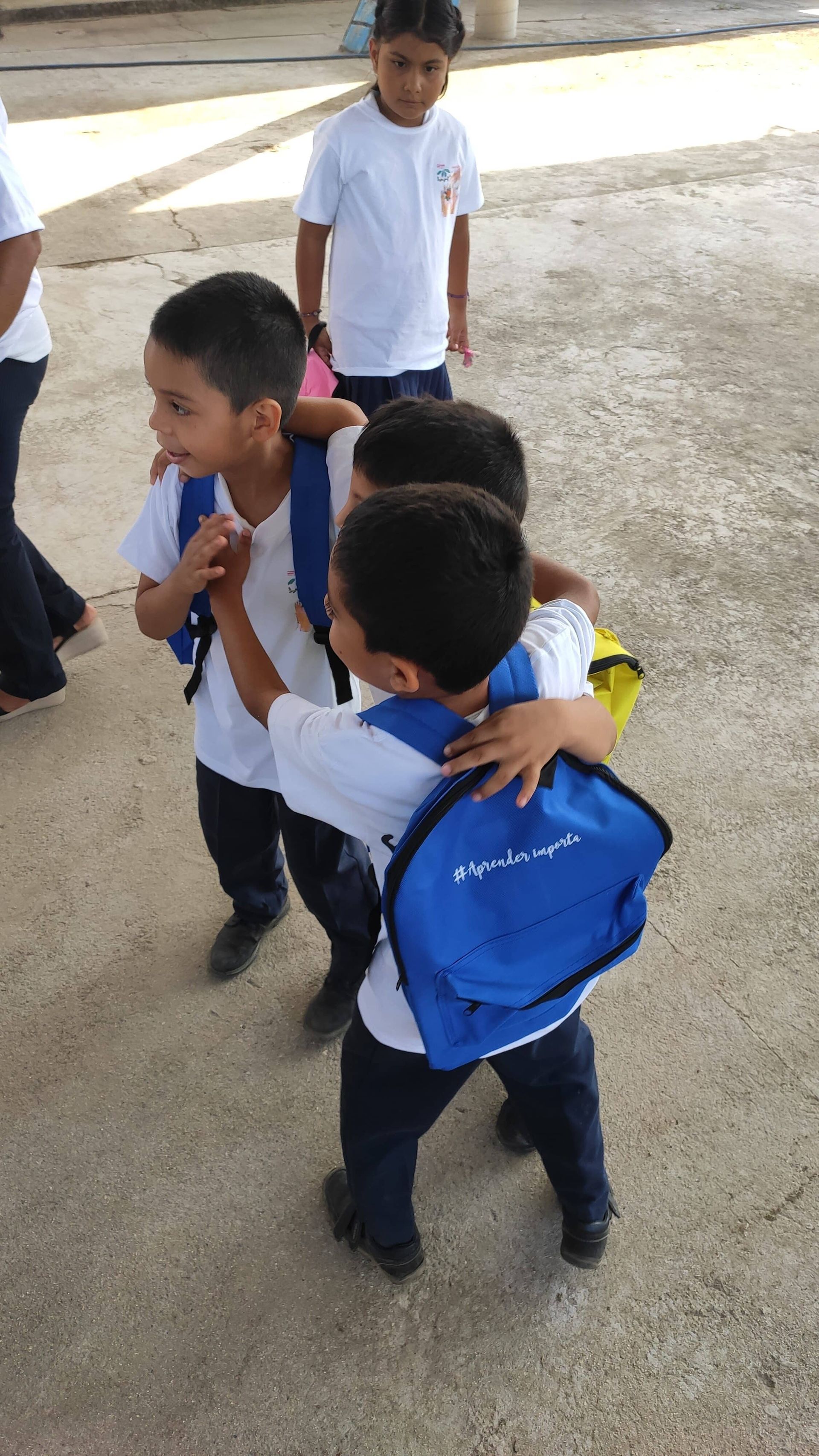 A group of young boys with backpacks are hugging each other.