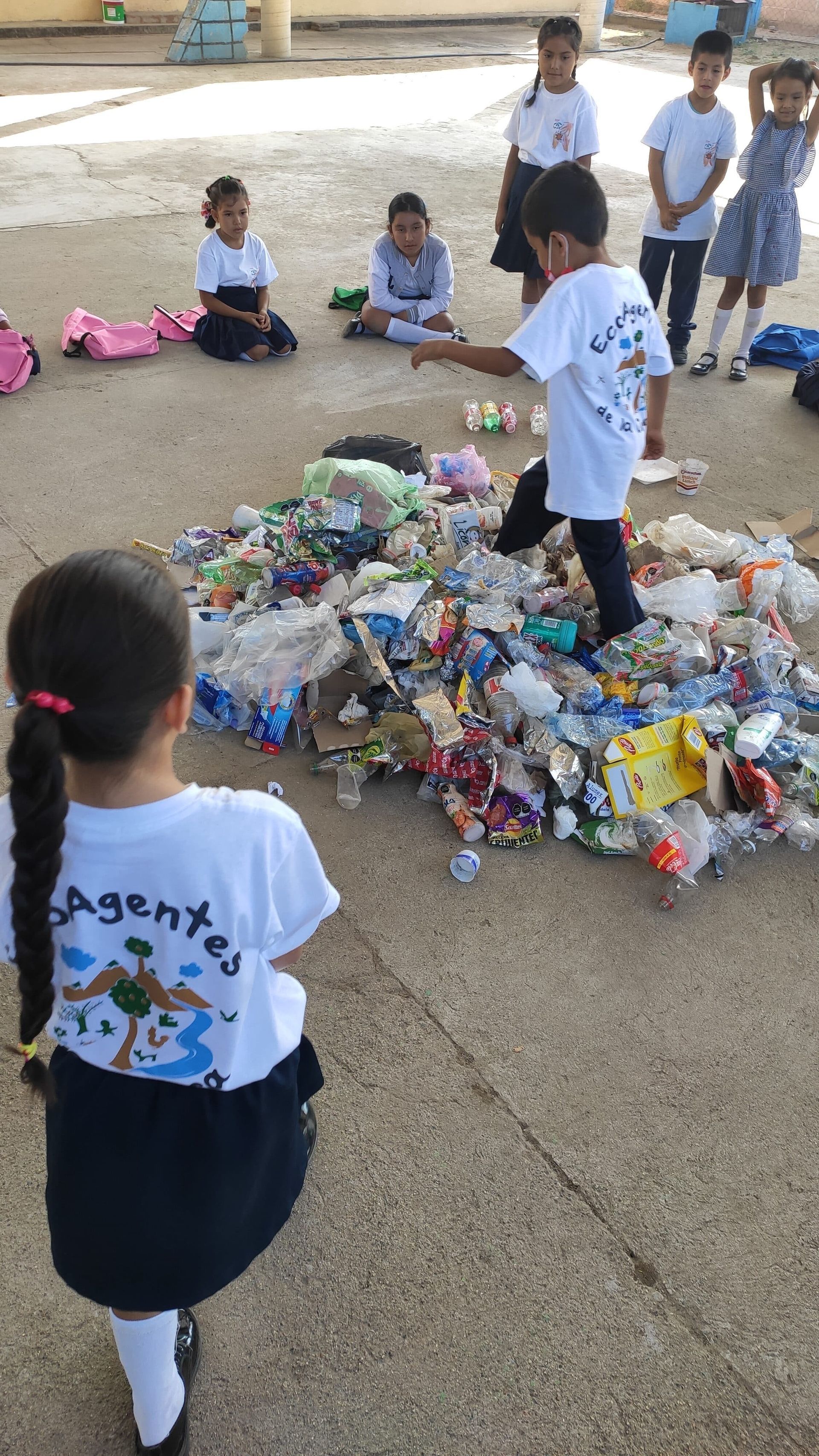 A girl is standing in front of a pile of plastic bottles.