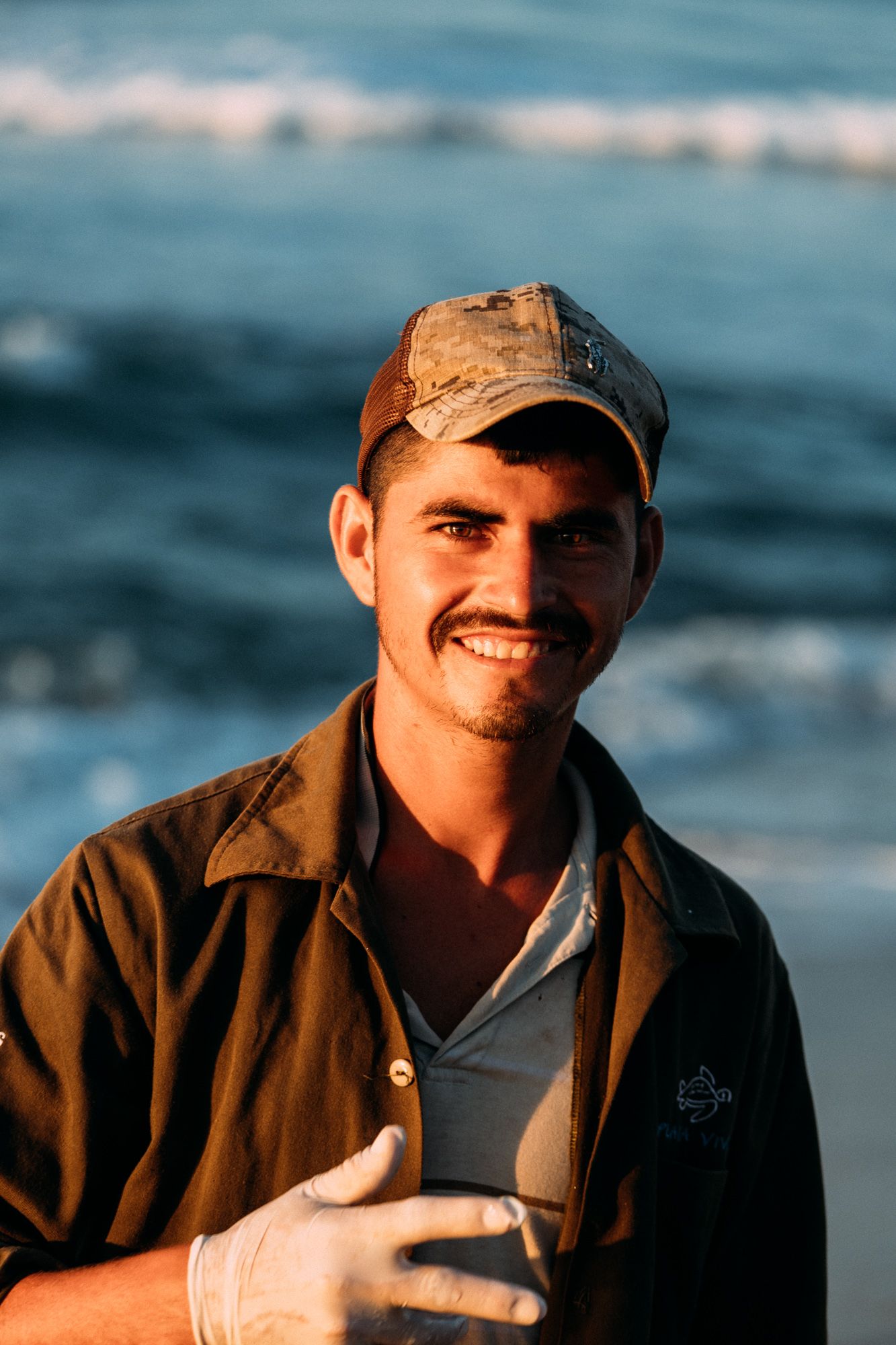 A man wearing a hat and gloves is standing on a beach.